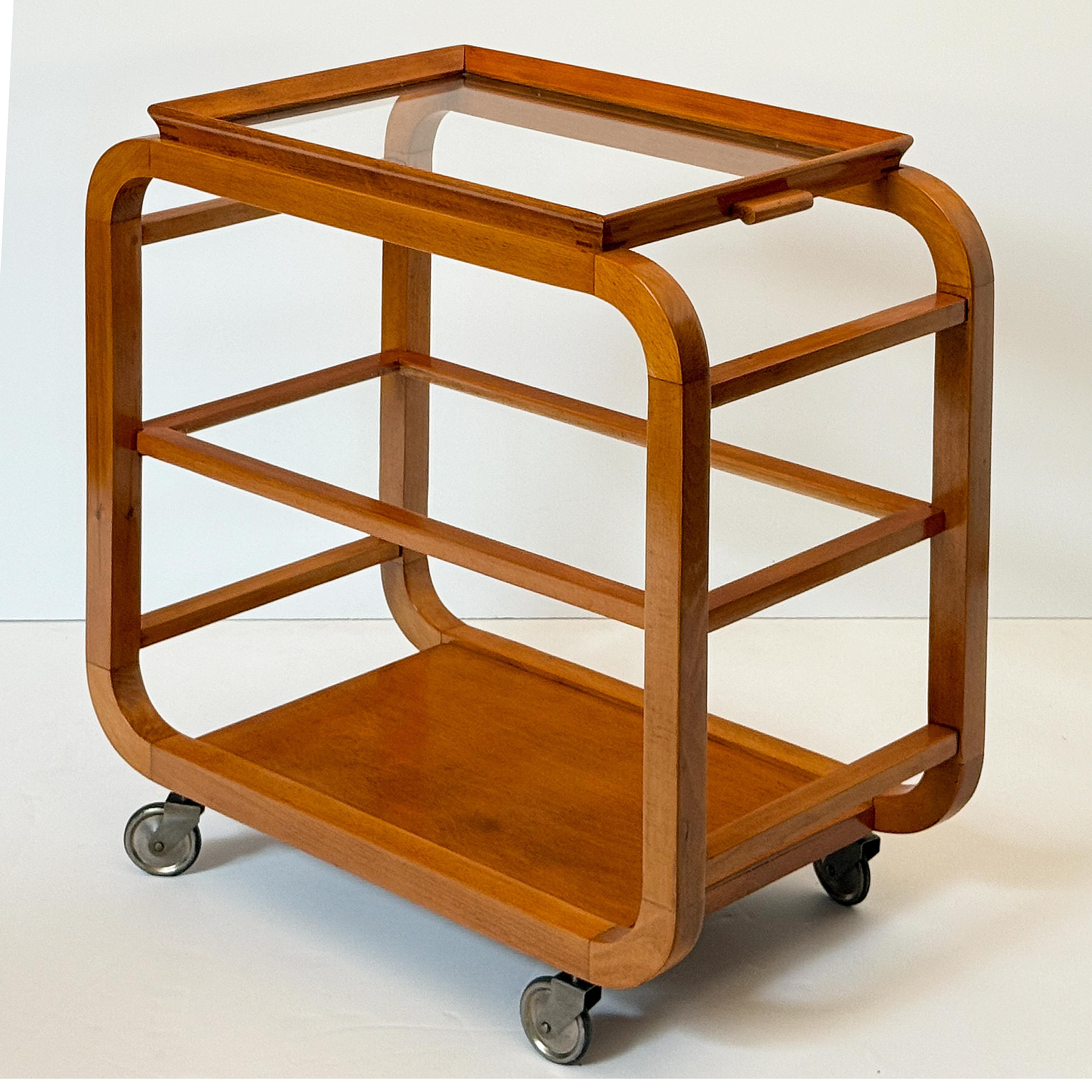 A fine Mid-Century Modern drinks cart or tea and coffee serving trolley table from Italy, featuring a removable rectangular tray top of glass with a moulded edge wooden surround, over a middle shelf of framed glass. Mounted to an elegant, curved
