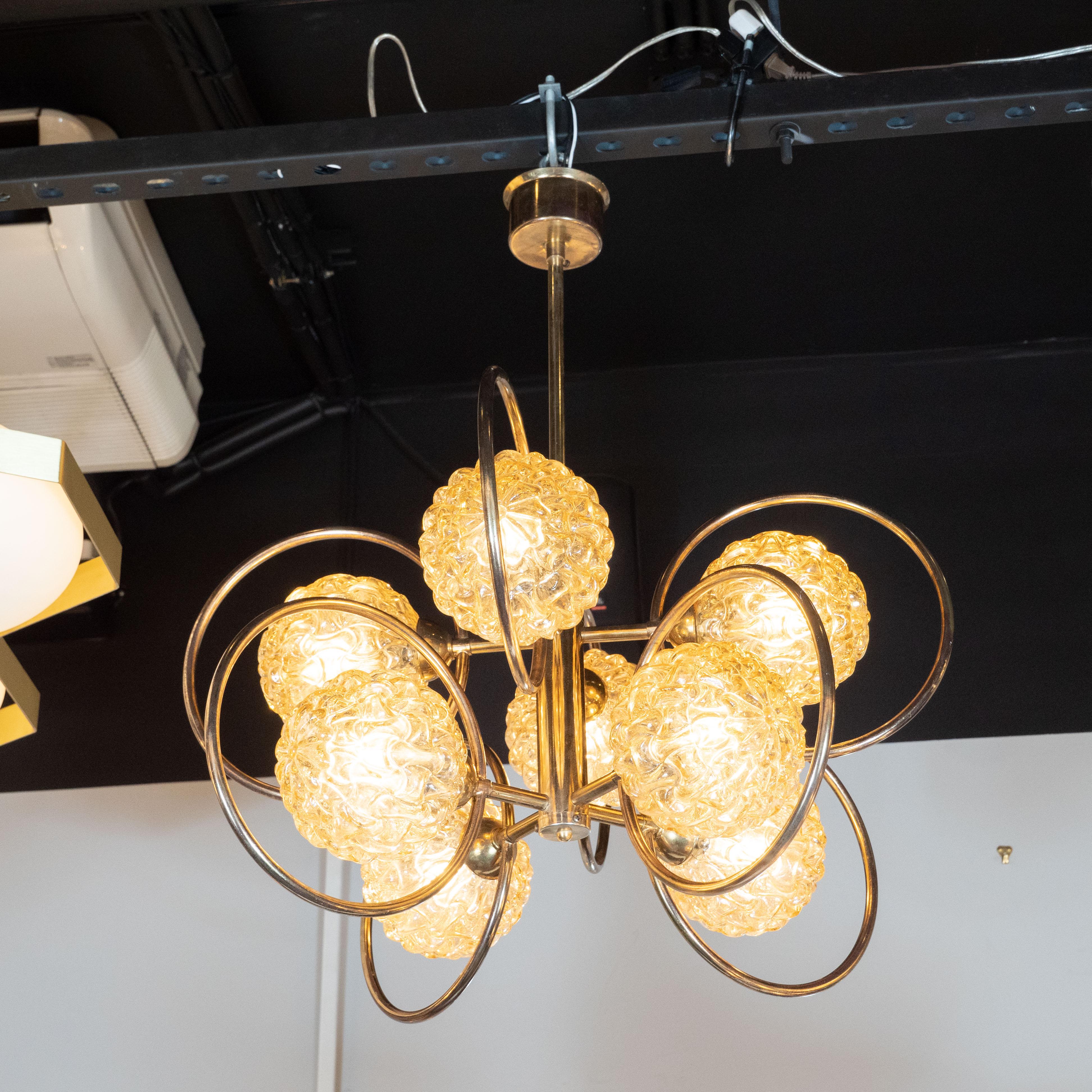 This Mid-Century Modern patinated brass chandelier was designed and produced in Italy, circa 1970. The fixture is suspended from a brass rod that connects to a central brass cylinder. Eight rods connect perpendicularly to this central cylinder, each