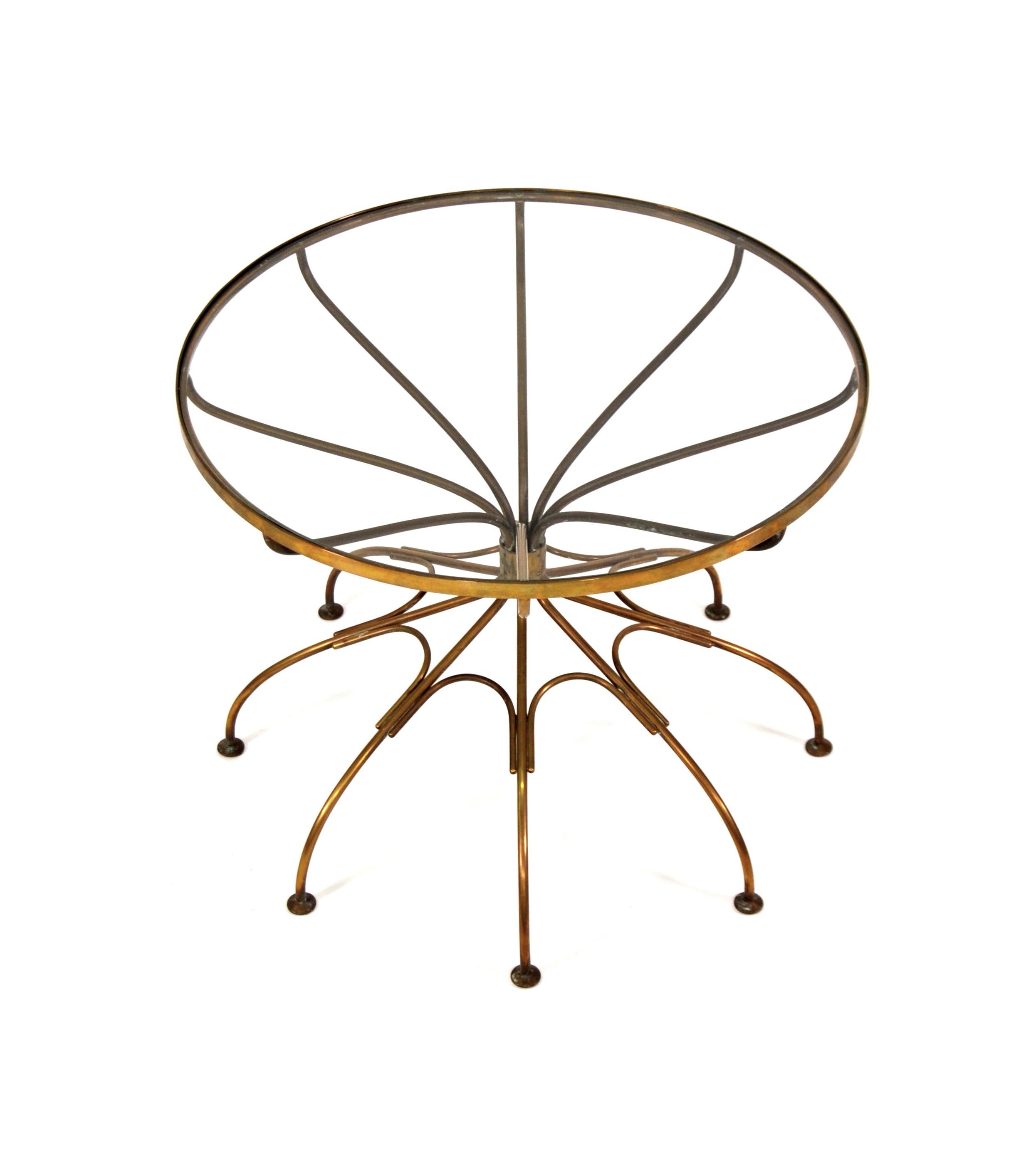 A whimsical vintage brass occasional table with a round, inset glass top, dating from the 1950s. The table features a solid brass frame shaped like a spider or the frame of an umbrella. A very unusual end table that can work well in many decors,