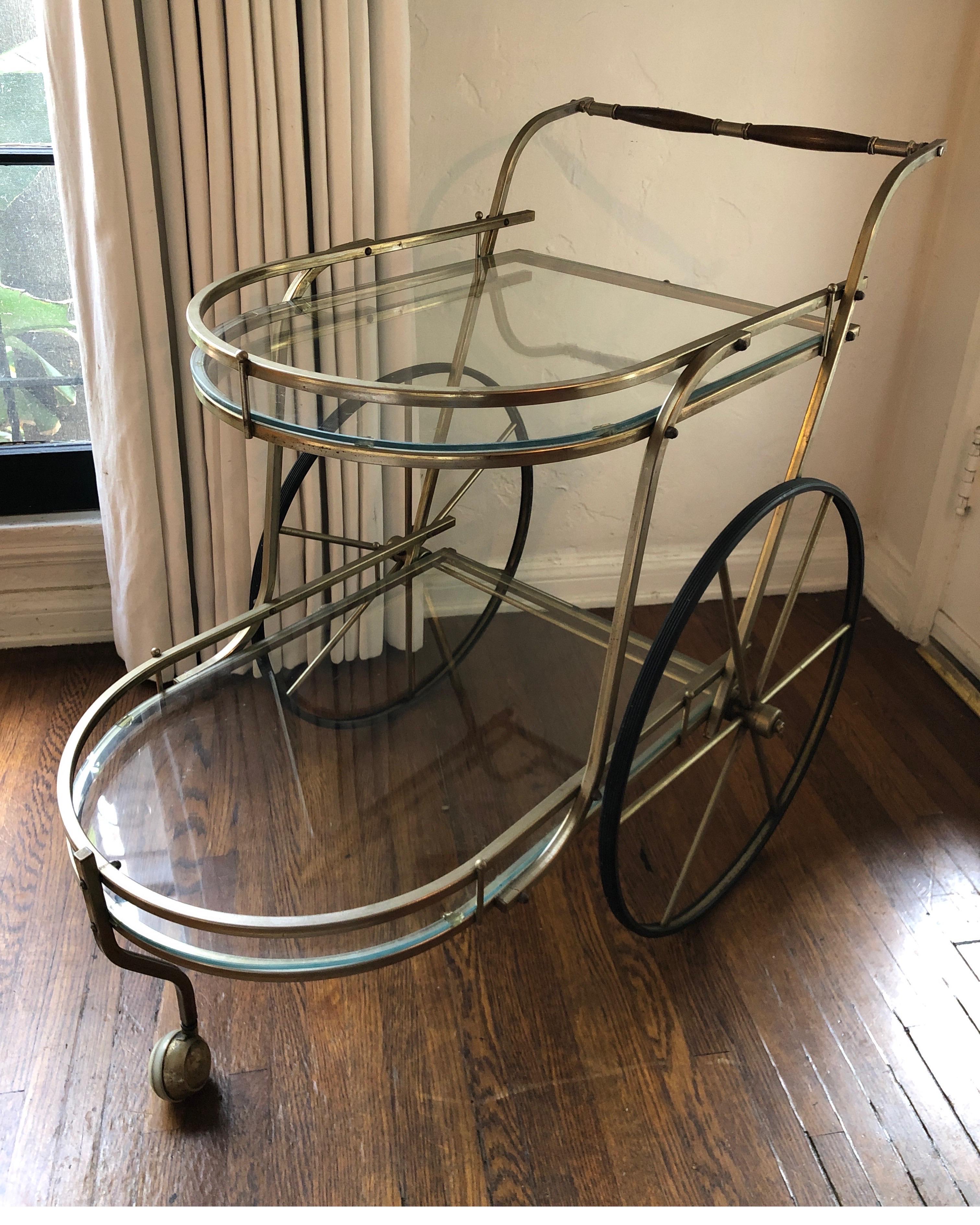 Large Italian two-tiered bar car. Brass finish with clear glass shelves. Two large wheels on each side that glide smoothly and one front wheel/caster.
Walnut handles.
Overall good condition with some signs of age on brass consistent with age.