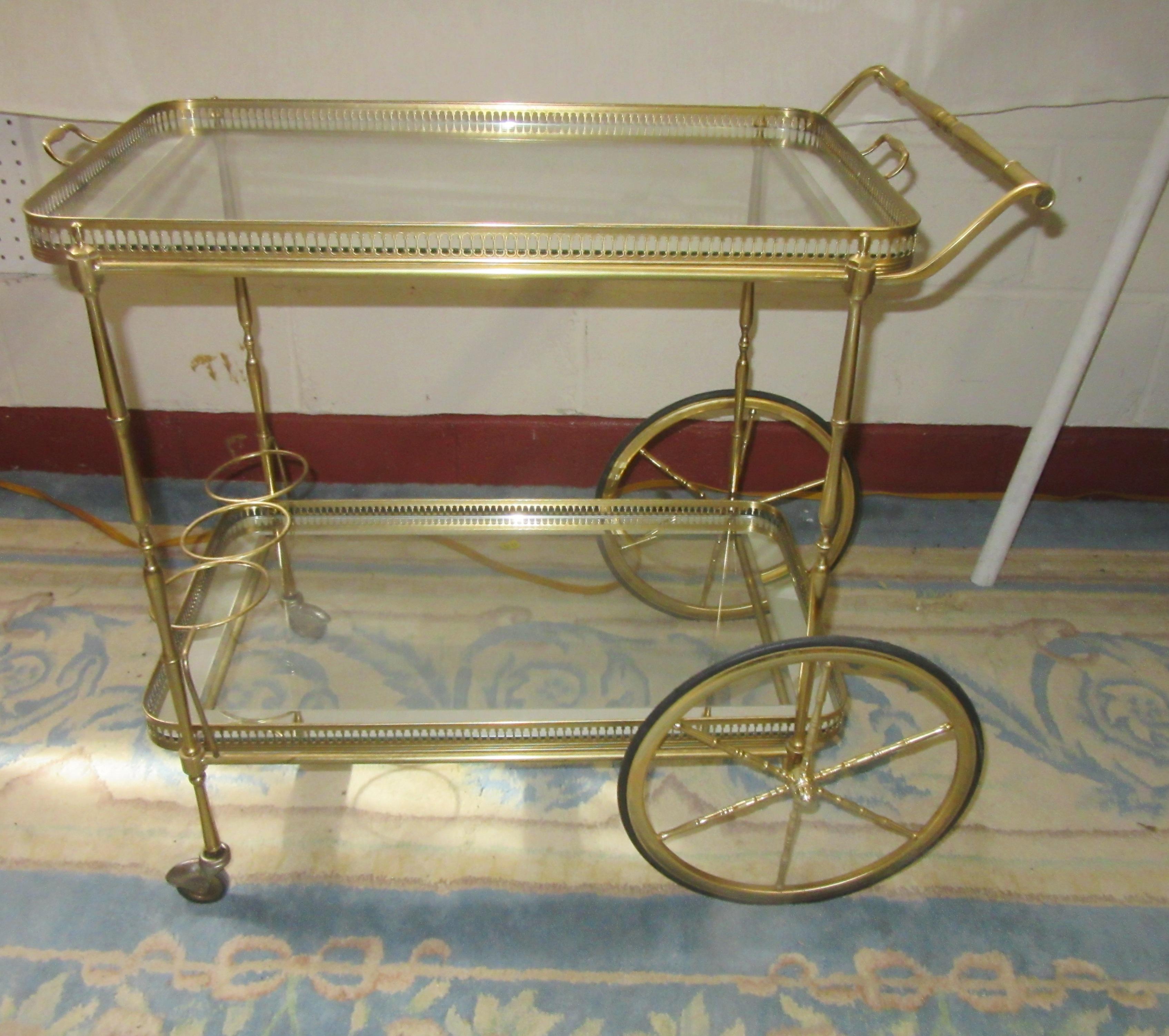 Mid-Century Modern Italian brass bar cart with two shelves. The top shelf has a removable tray with a glass shelf and a silver border. The bottom shelf has a glass shelf with a silver border and a holding place to store 3 bottles.
In great vintage