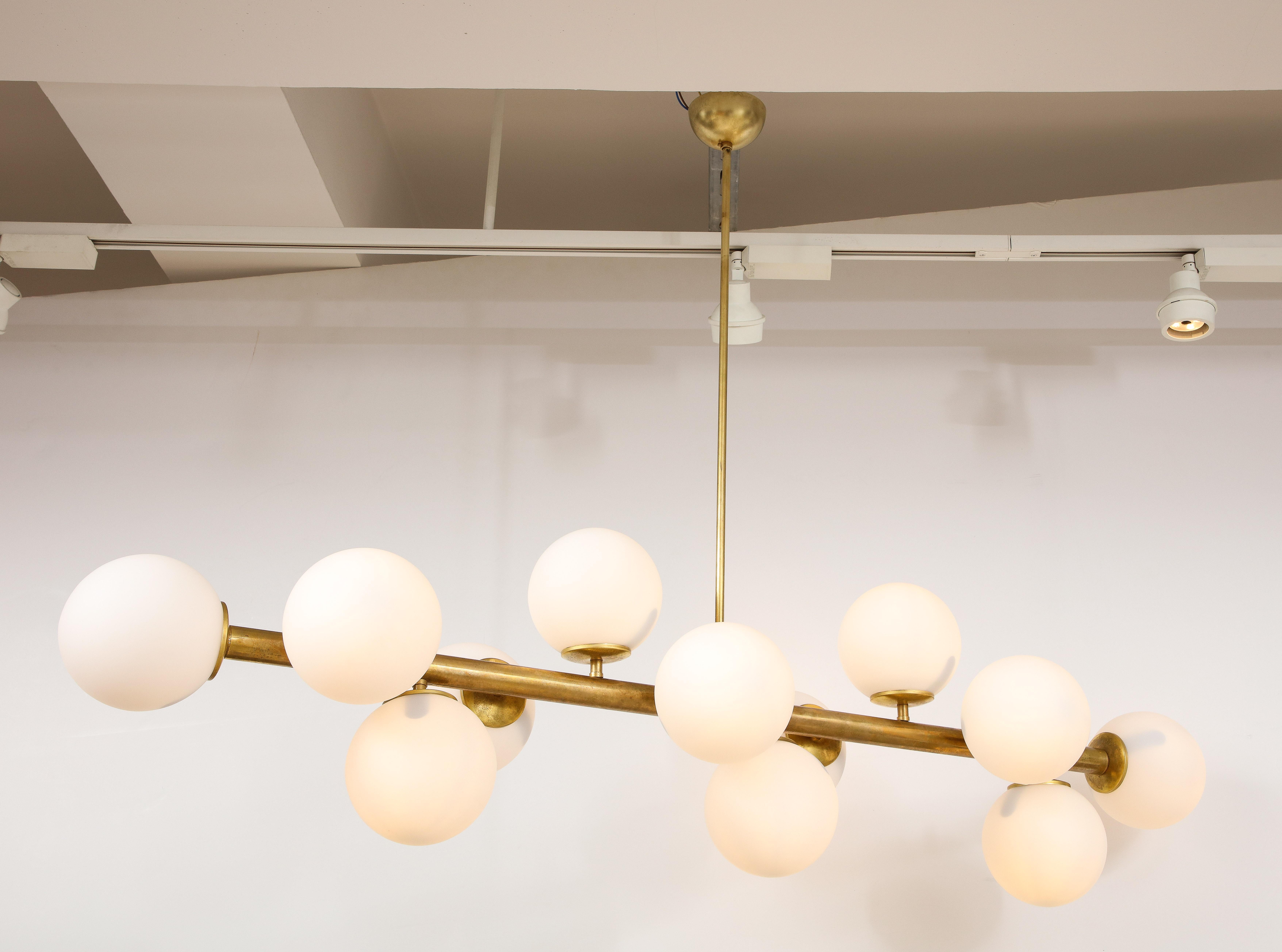 Italian Mid-Century Modern horizontal brass chandelier with twelve opaline glass globe light fixtures. A dramatic piece for any interior style. The brass with original warm patina. Re-wired for US standards. 
Italy, circa 1960 
Size: 34