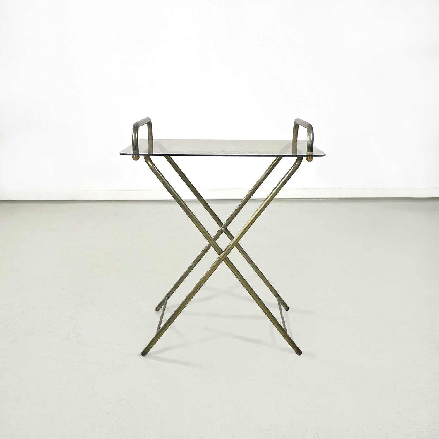 Italian mid-century modern brass structure and crystal top service table, 1960s
Rectangular service or coffee table. The structure is in brass rod and is foldable, it has a small chain that blocks it. The top is in colored crystal, it has two brass