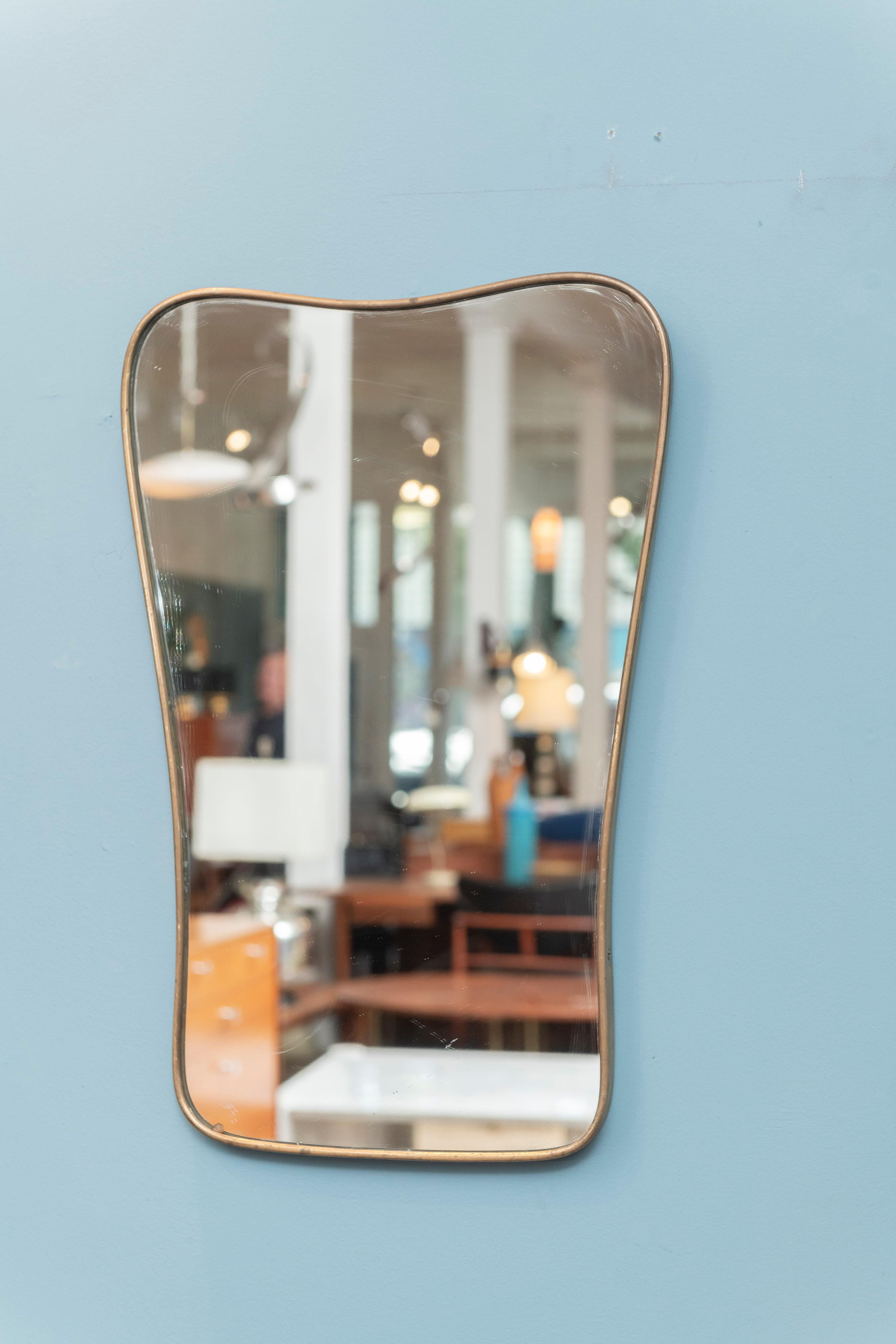 Italian Mid-Century Modern brass wall mirror. Attractive dog bone curved shaped frame in a patinated brass with original mirror plate. Perfect for a hallway or small bathroom, ready to install.
