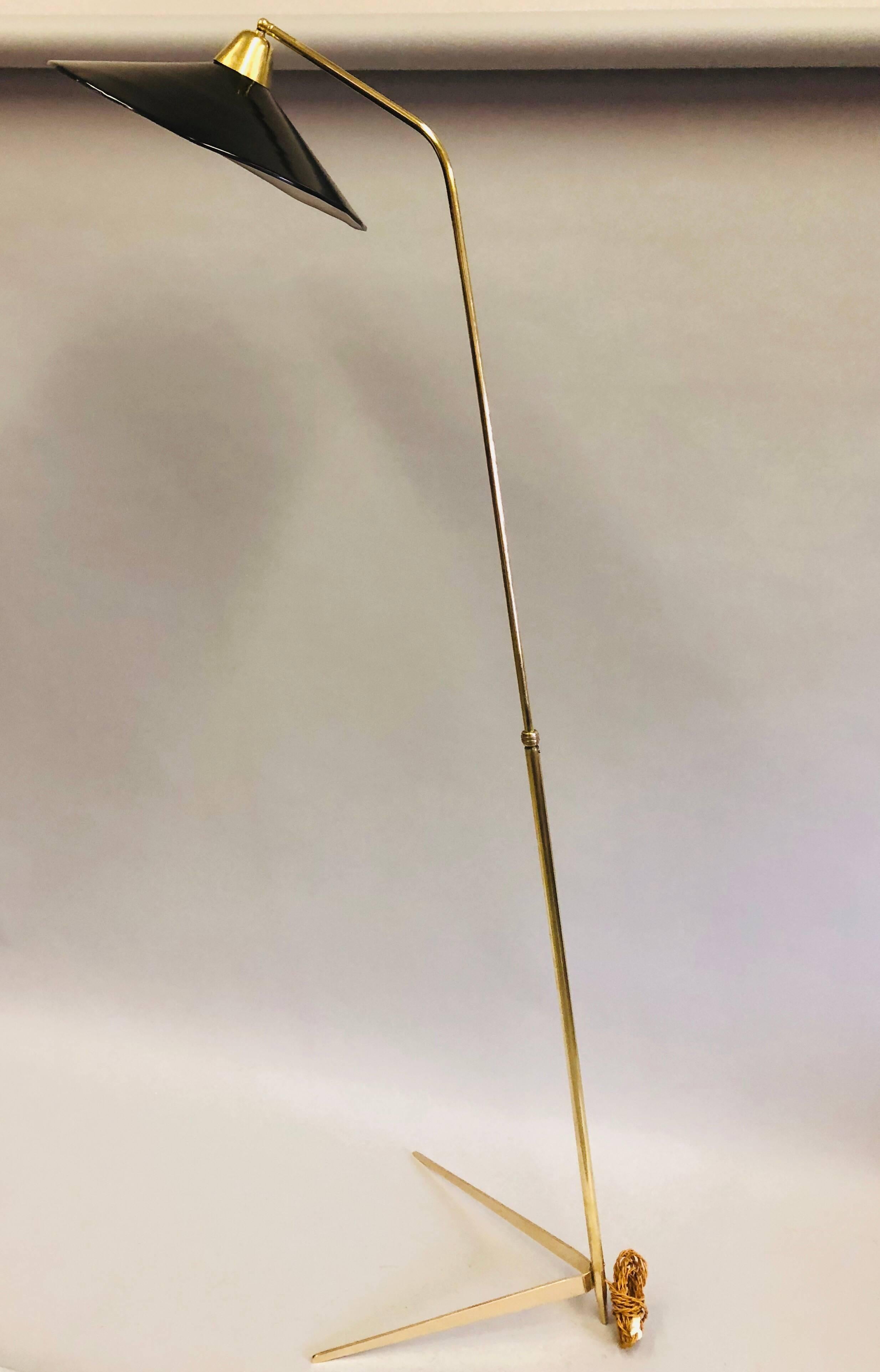 An important sculptural, Italian Mid-Century Modern floor lamp in solid brass with an elegant, tapering, tripod base in the form a hairpin and round, black enameled metal shade. The stem and shade cantilever over the base at a delicate angle.