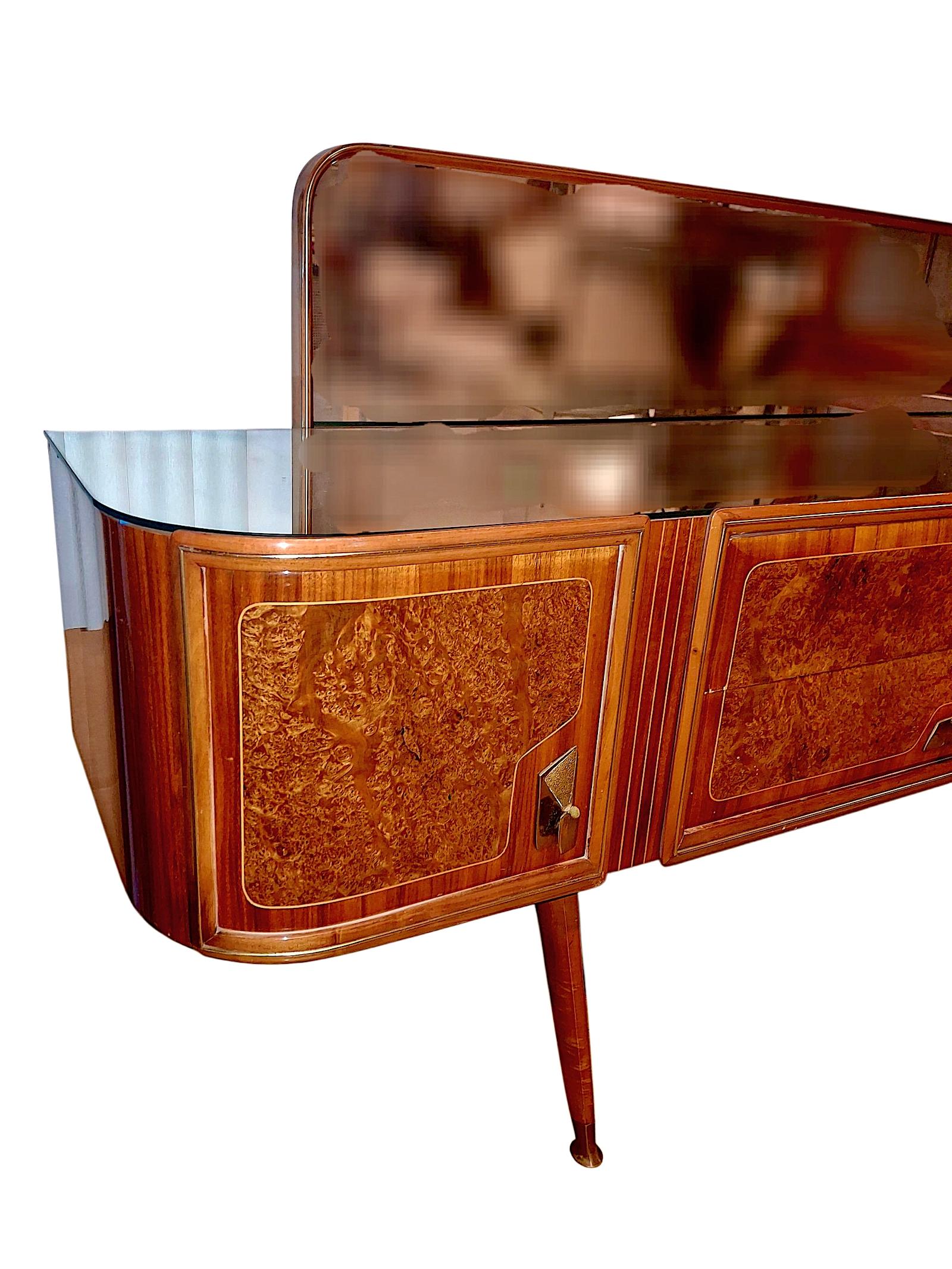 On offer is a curved rectangular commode with a gleaming French polish finish by Italian architect, designer, essayist and academic Carlo De Carli (1910-1999). The mirrored section sits atop the two-door, burl-veneered case with brass inlay, two