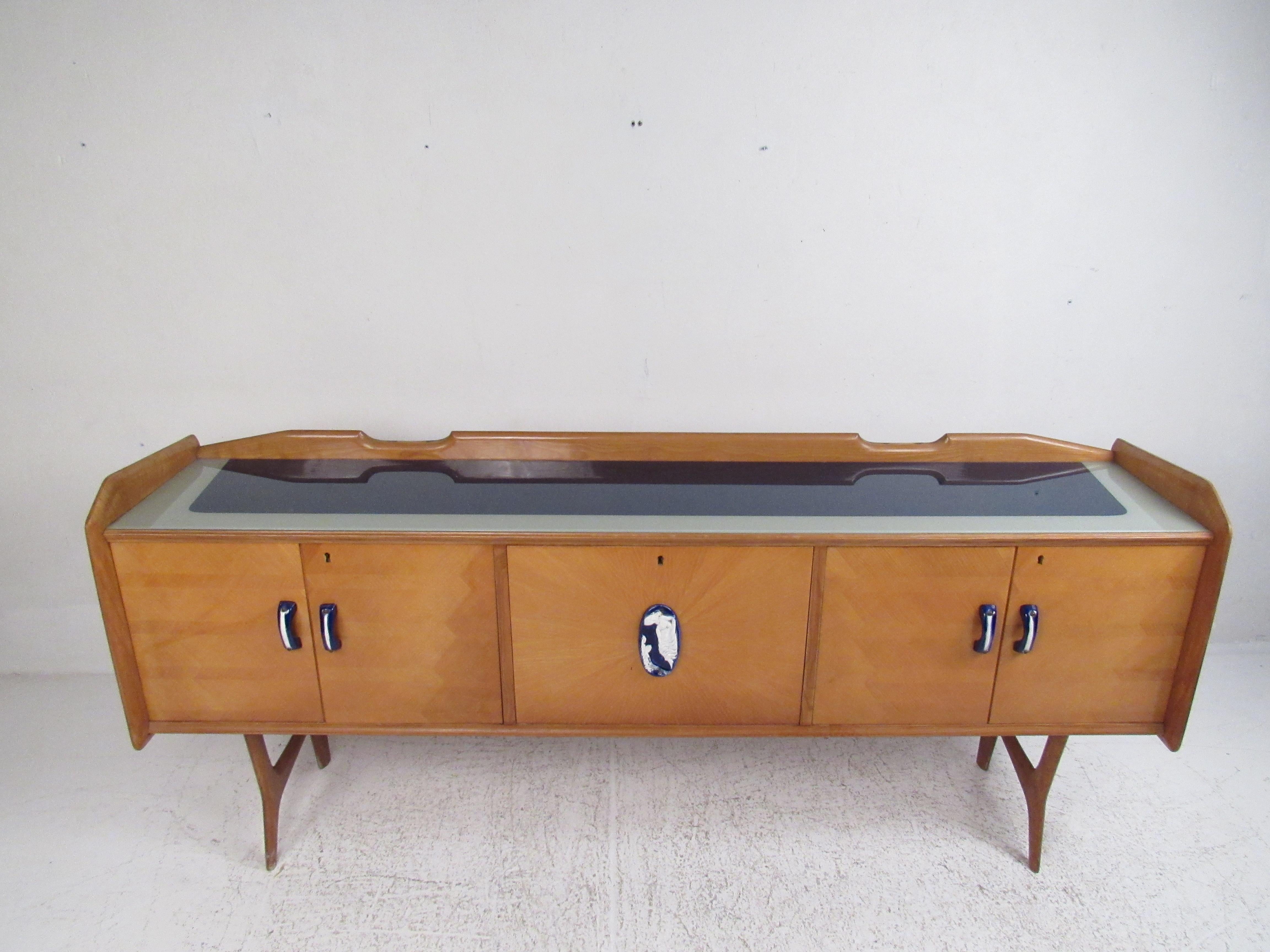 This stunning vintage modern sideboard features cobalt handles on the cabinet doors. An unusual Ico Parisi style design that has a two-tone glass top. The raised edges along the top add to the mid-century appeal. This sleek case piece offers plenty