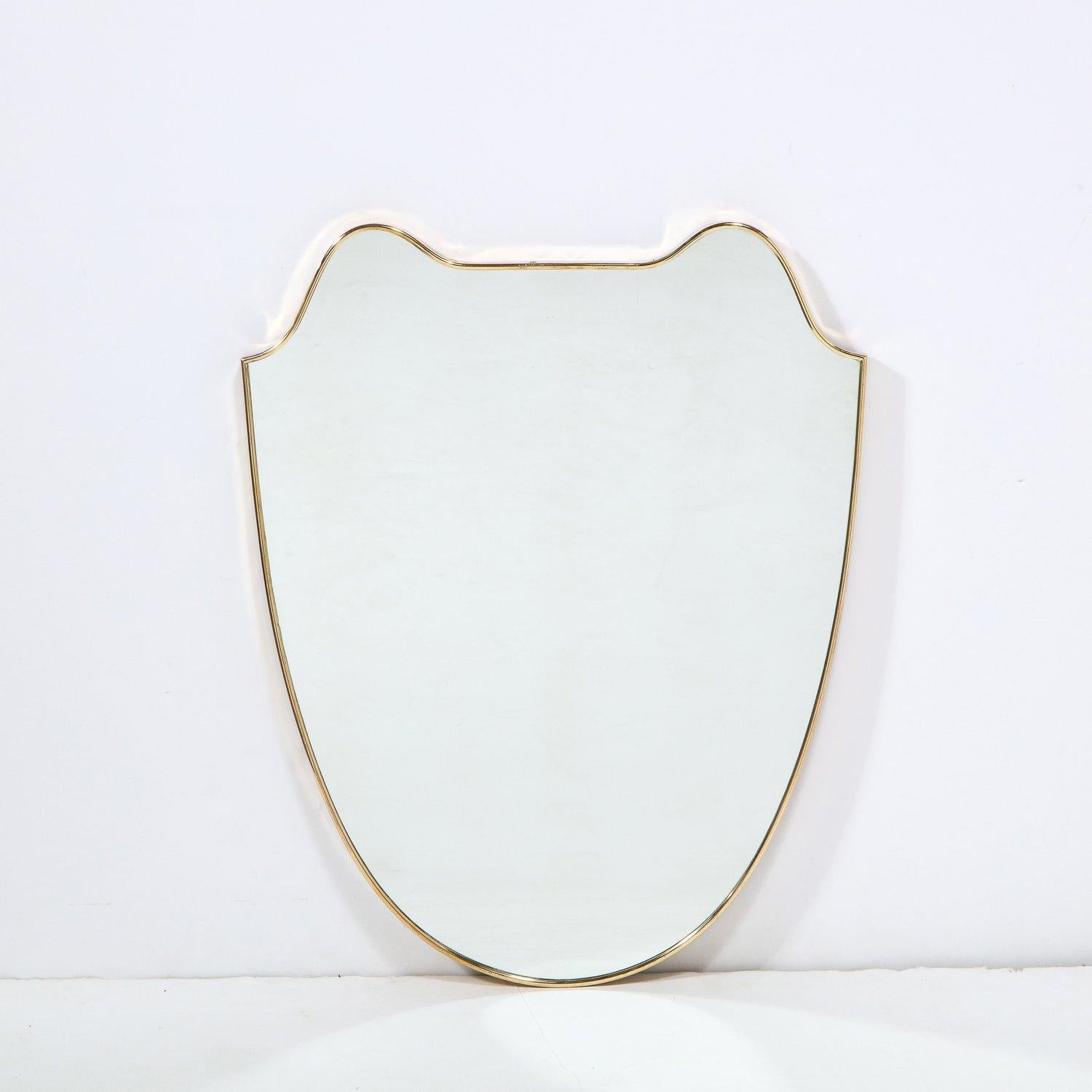 This elegant and austere Mid-Century Modern mirror was realized in Italy, circa 1950. It offers curvilinear forms with rounded shoulders in polished brass. The frame offers a subtle subtle elegance surrounding this unique form. With its clean