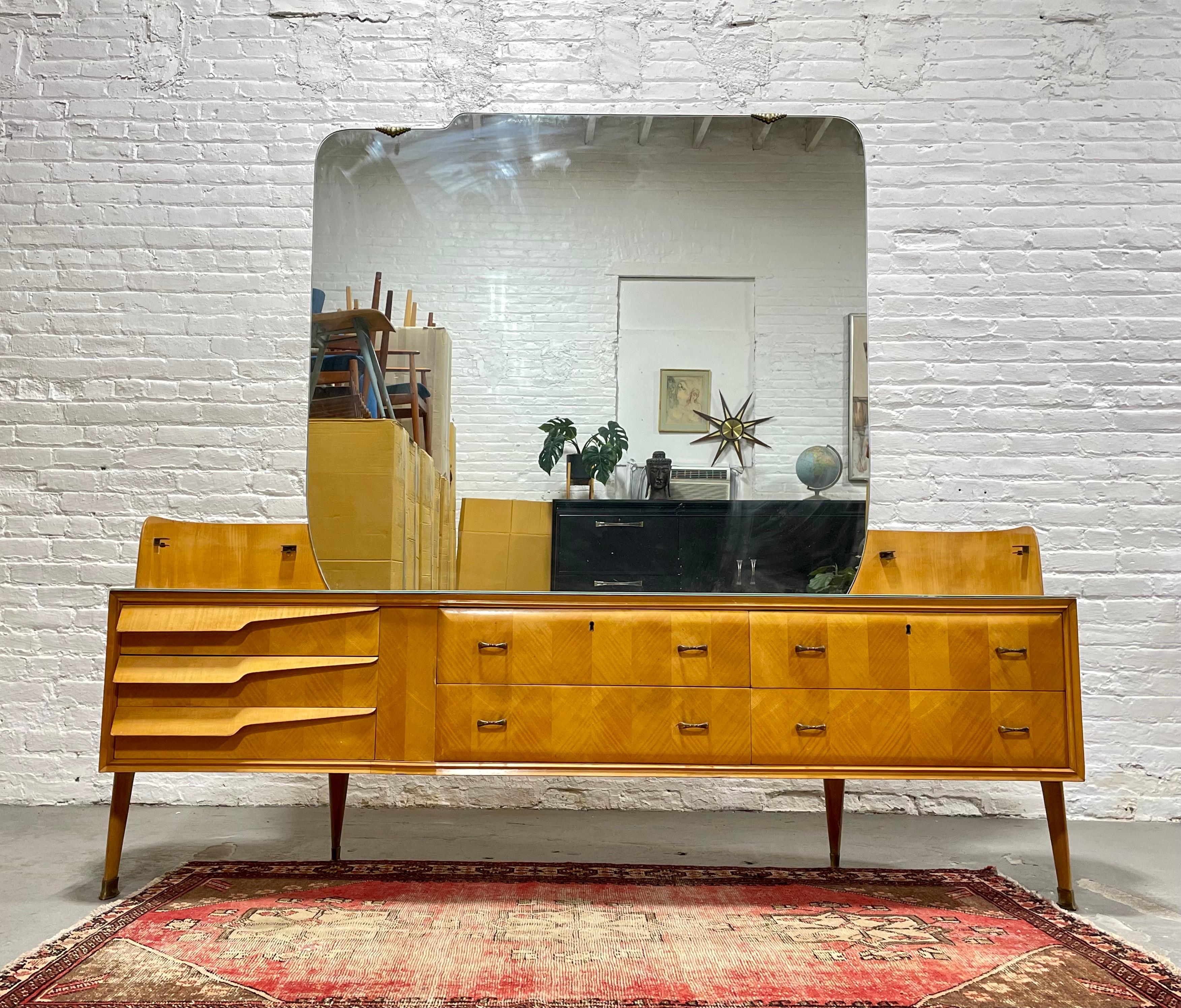 Italian Mid Century Modern Long Dresser + Large Mirror, c. 1960’s.  This incredibly unique piece consists of a 7 drawer maple wood dresser with a faux pink marble protective top, two glass shelves and a large mirror at the center.  The legs are