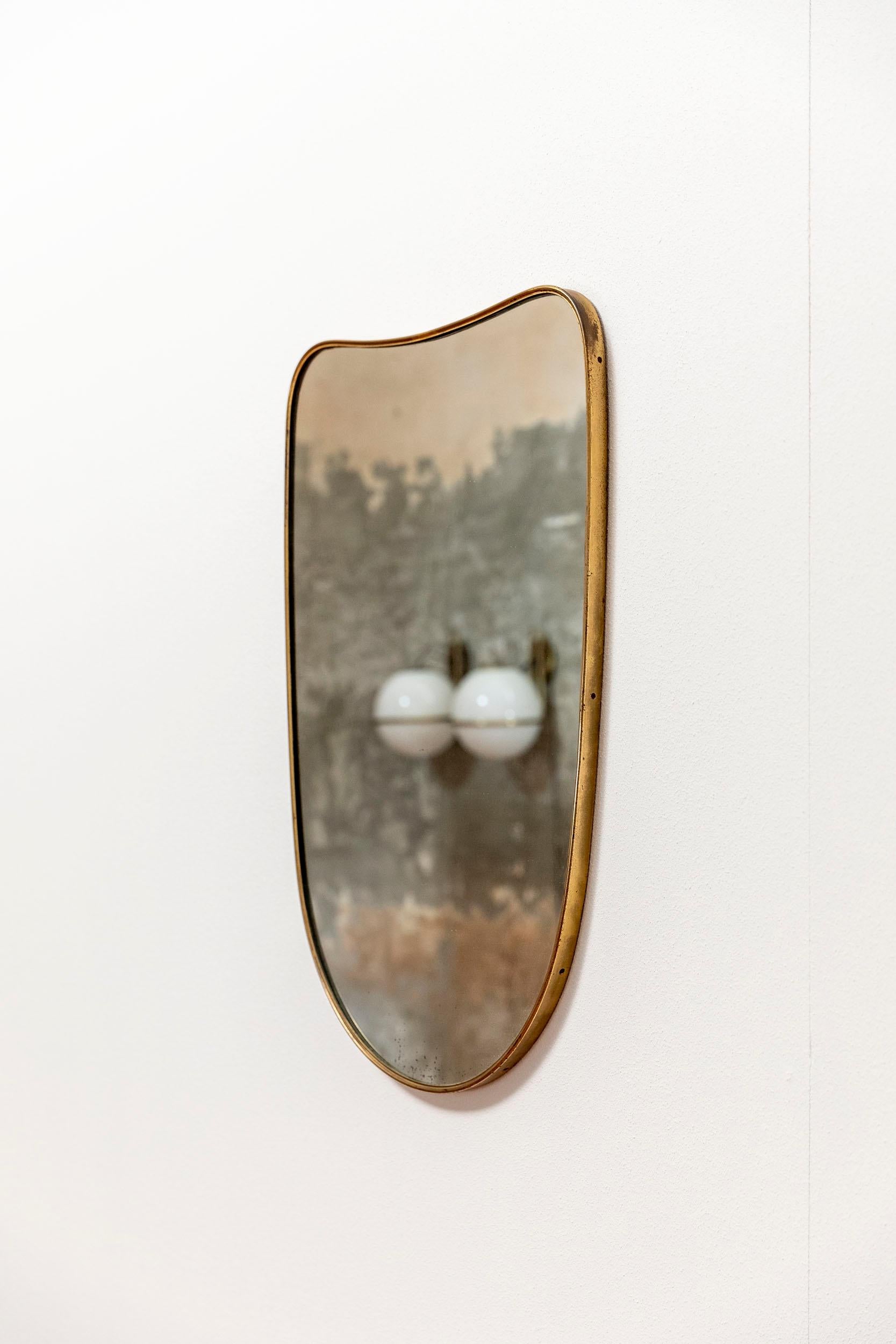 Italian Mid-Century Modern mirror inspired to Gio Ponti. 
Brass frame with elegant shaped and rounded corner.