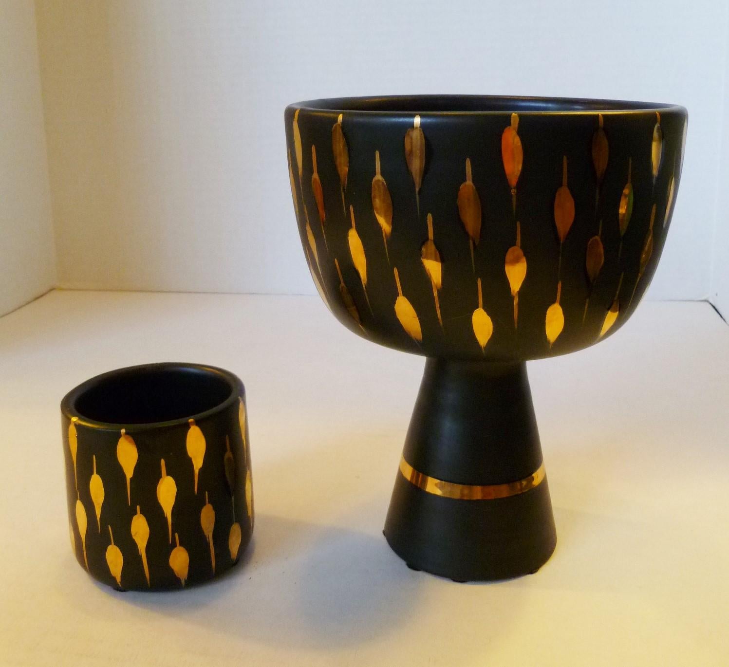 Elegant and swank 1960s Italian pottery vessels with black glaze highlighted with a gilt gold teardrop pattern. Consisting of a shorter Tumbler shape vessel and a taller footed Vessel.
Measurements: Tumbler 3 inches in diameter x 2 7/8 inches high.