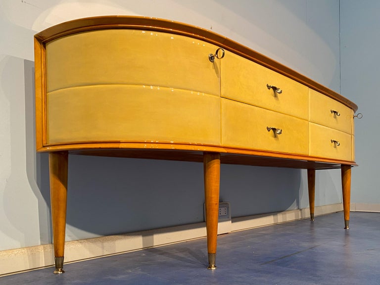 Italian midcentury modern sideboard, buffet chest of drawers in parchment and maple with two side doors and four drawers, in Paolo Buffa style. It has an elegant movement of the lines on the front with glass mirror top.Tapered legs with final brass