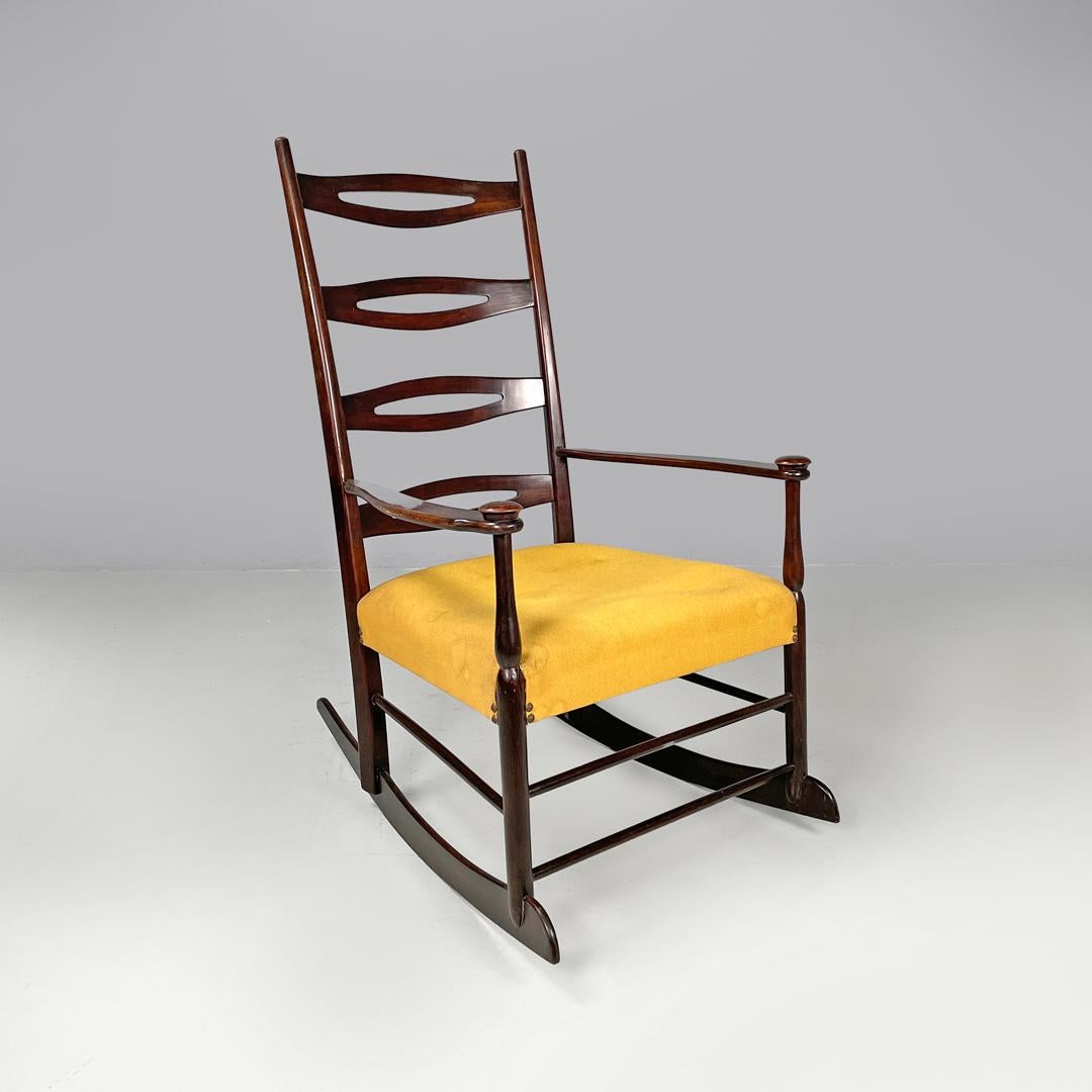 Italian mid-century modern rocking chair in wood and mustard yellow fabric 1960s
Wooden rocking chair with padded seat in mustard yellow fabric with brass studs. The backrest has strips with decorative elongated holes, the armrests follow curved