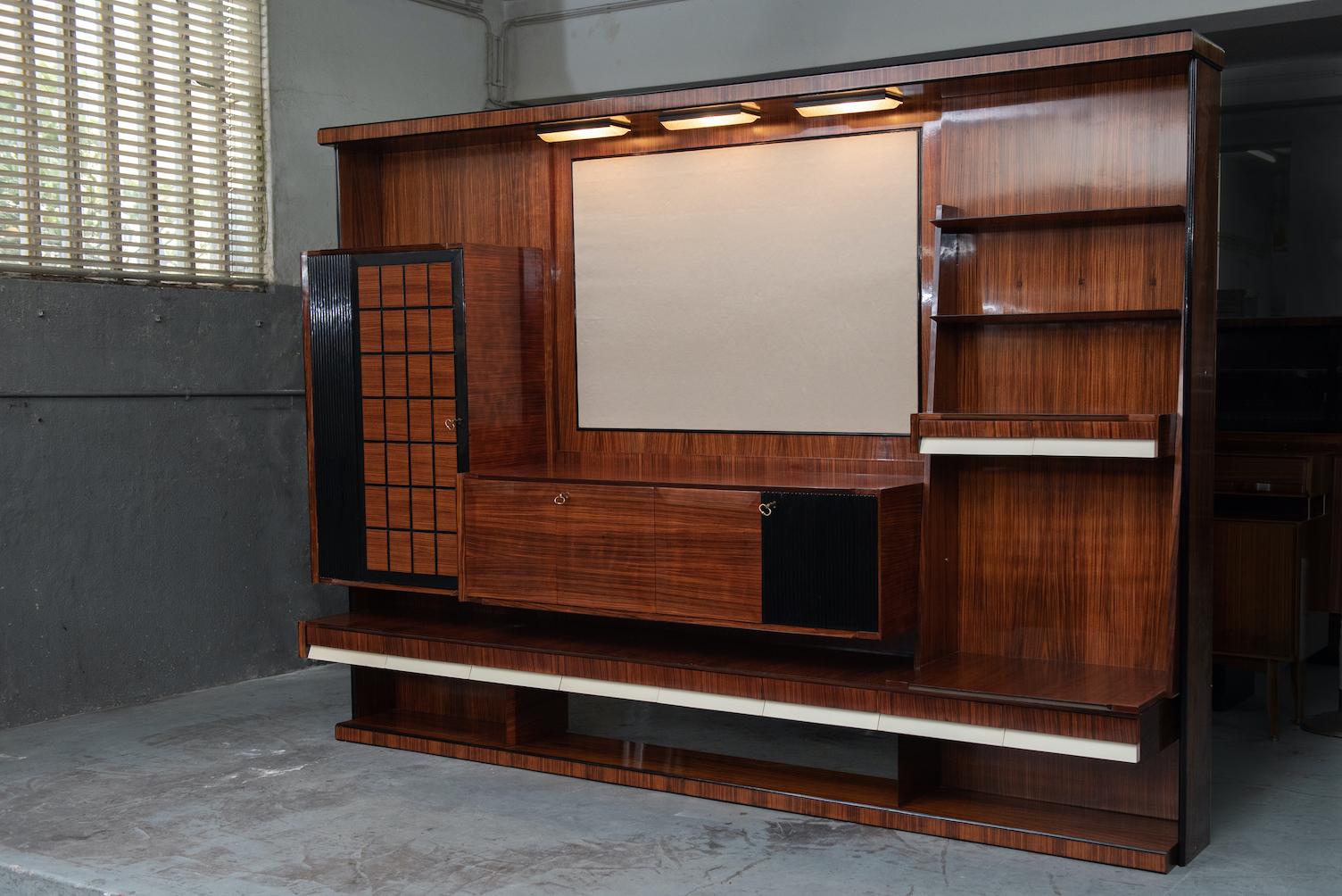 Italian Mid-Century Modern rosewood large living room bookcase with storage, white lacquered details on the drawers and a fabric upholstered panel to put the TV or a painting, is has also three lamps over the upholstered panel.