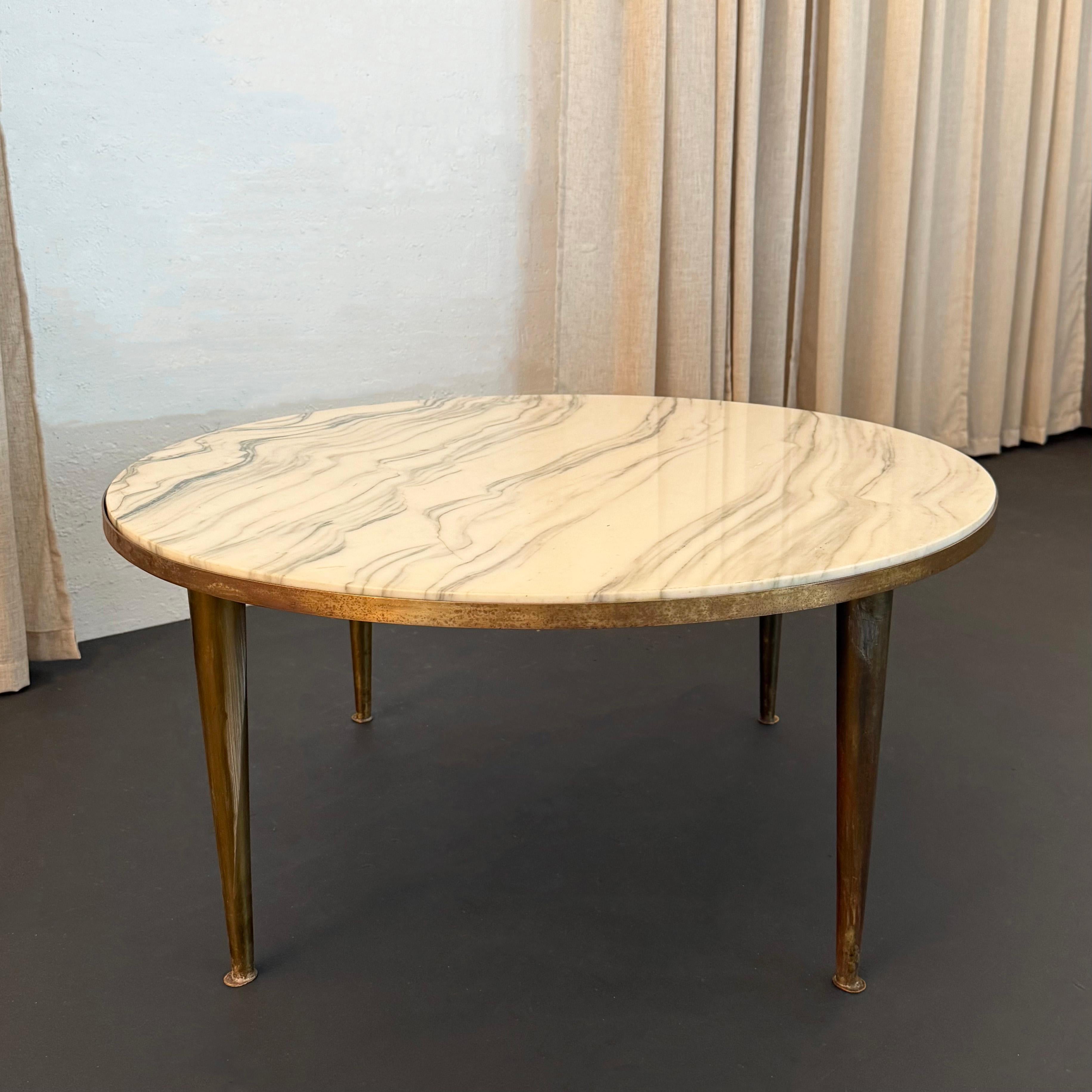 Cette table basse chic de style italien moderne du milieu du siècle brille par ses détails subtils. La table présente un épais plateau rond en marbre blanc avec des stries grises exceptionnelles qui repose à l'intérieur d'une bordure en laiton sur