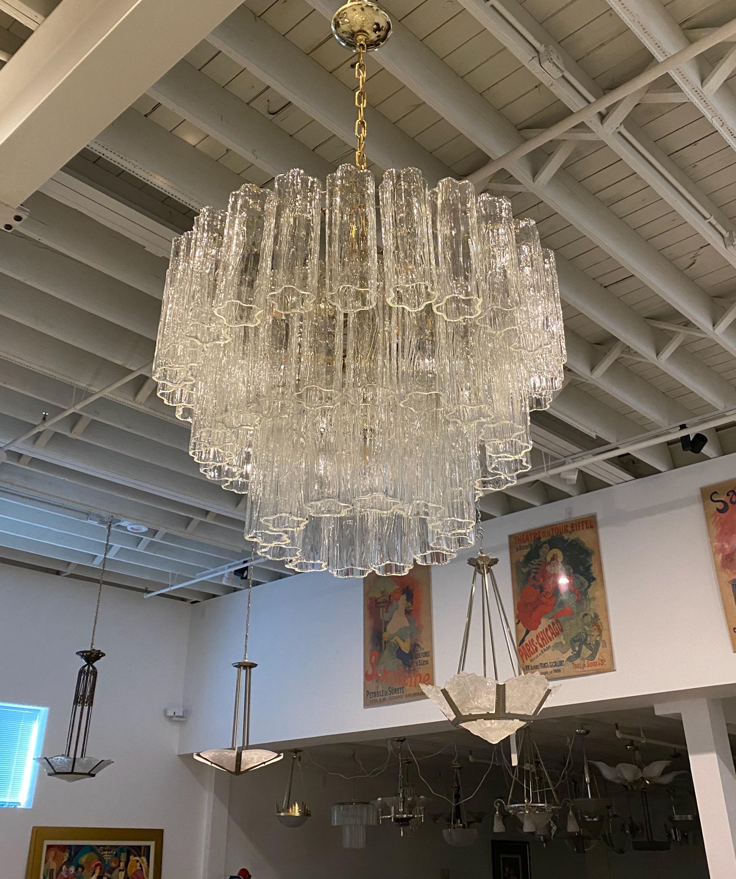 Mid-Century Modern three-tiered round chandelier. Consisting of tronchi cylindrical glass pieces. Each piece is hand blown and has a star or floral shape. The glass tronchi hangs from a brass frame as pictured. Any amount of chain can be added for