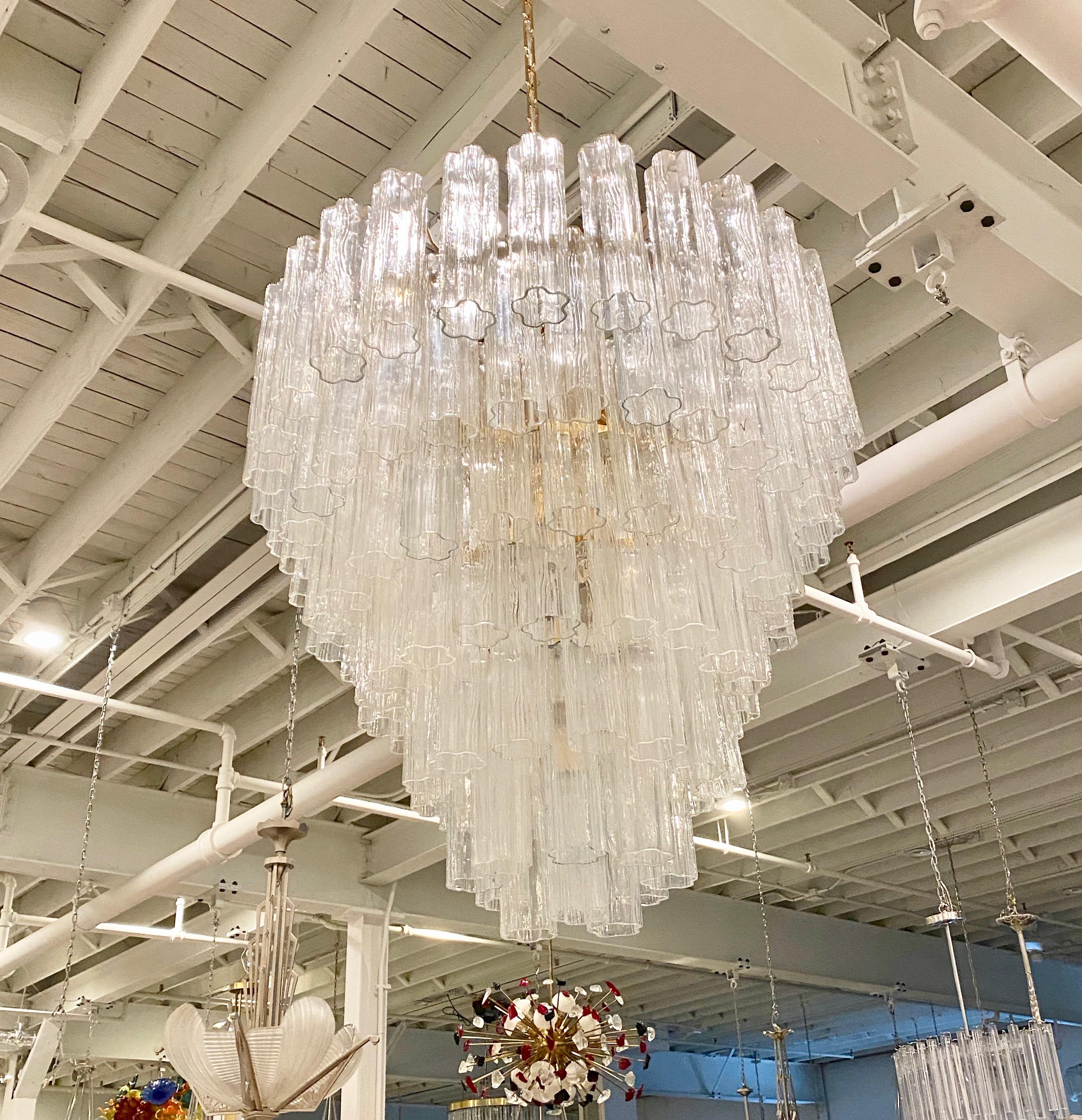 Mid-Century Modern round tiered chandelier. Consisting of tronchi cylindrical glass pieces. Each piece has a star or floral shape. The glass tronchi hangs from a brass frame as pictured. Any amount of chain can be added for custom hanging length.