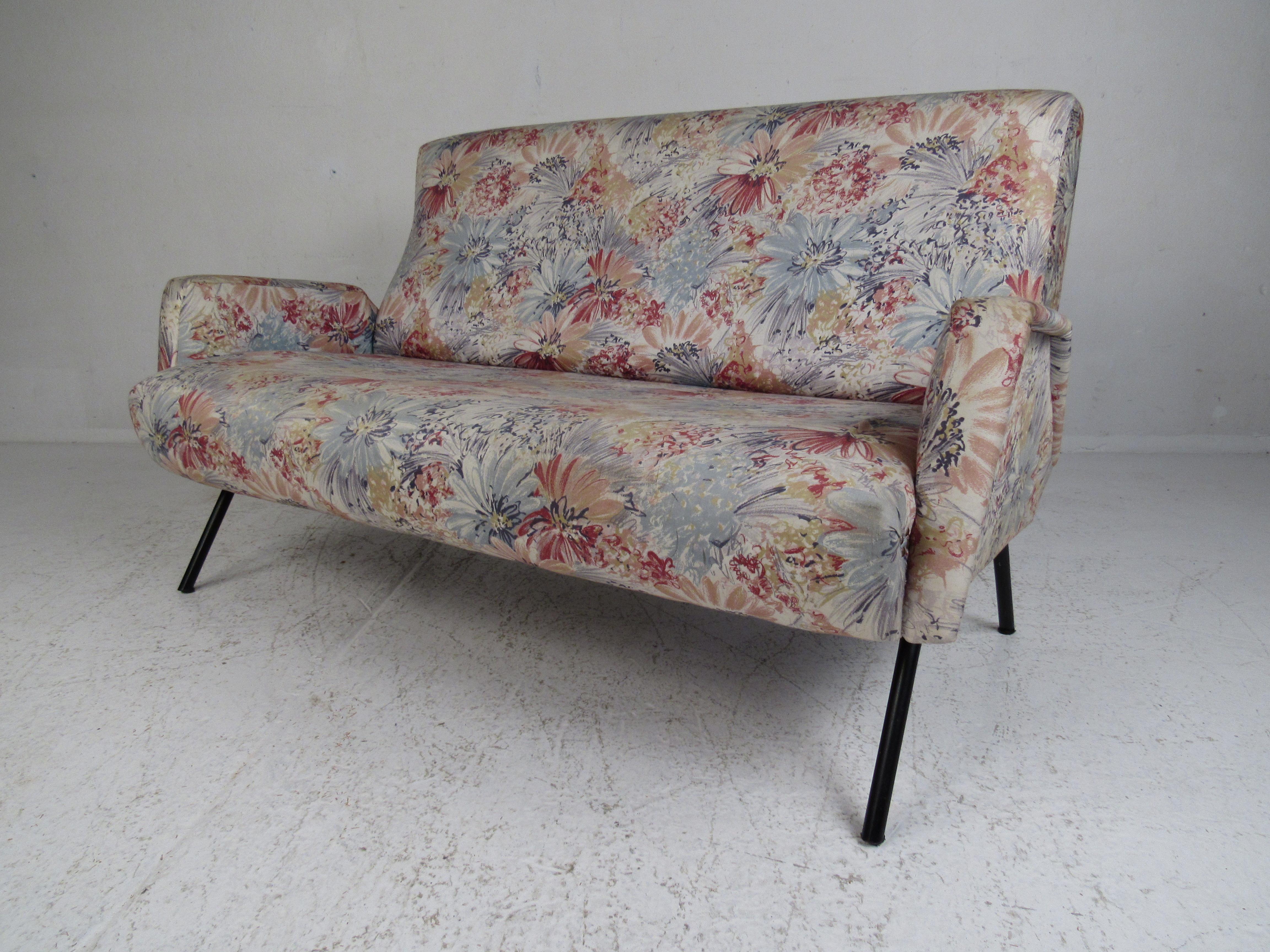 This stunning vintage modern sofa features unique sculpted armrests and a metal base. A stylish and comfortable design with thick padded seating covered in decorative floral upholstery. This wonderful midcentury settee is sure to make a lasting