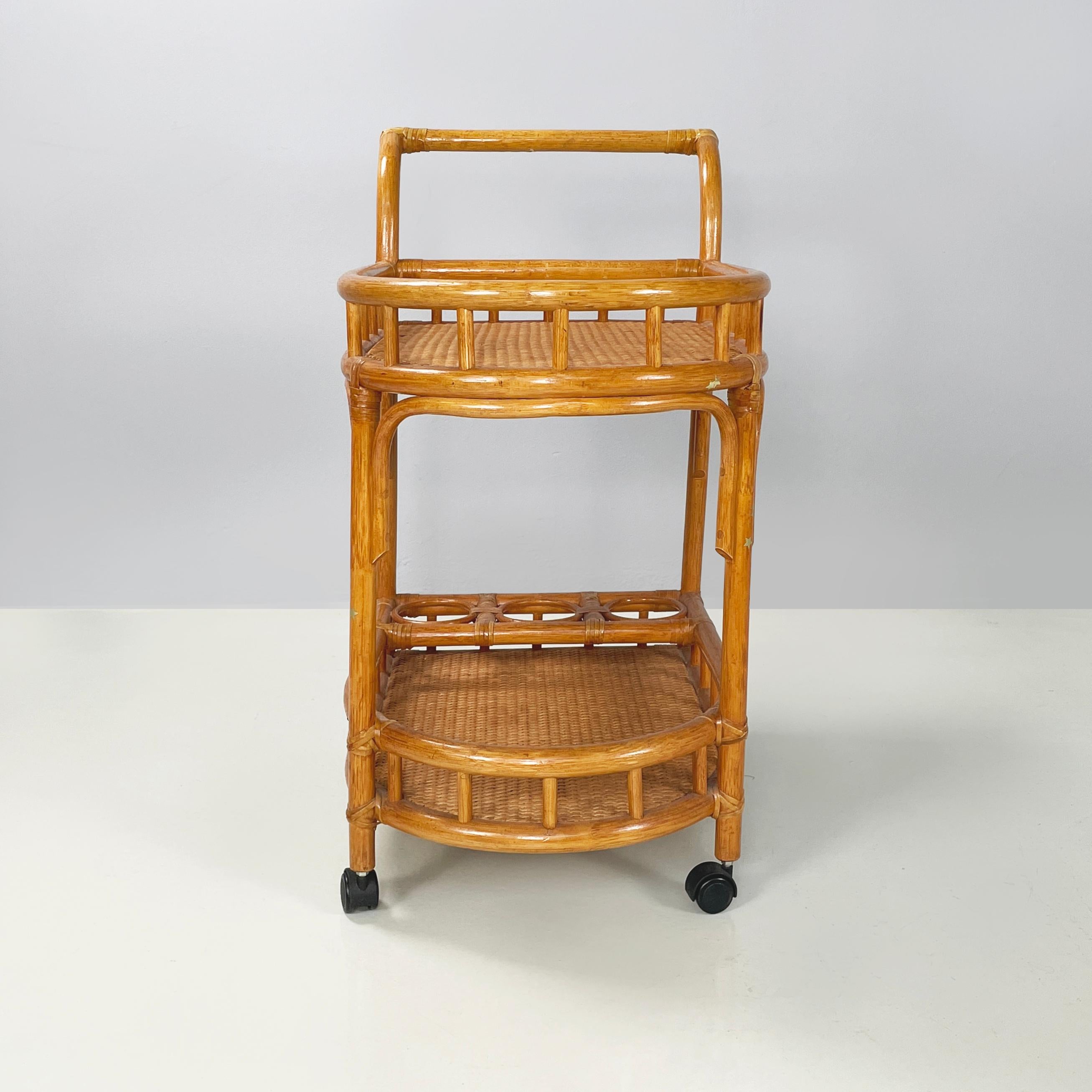 Italian mid-century modern Double-shelf and bottle holders cart in rattan bamboo, 1960s
Double-shelf food cart in rattan and curved bamboo. The two shelves have a rounded side with woven rattan interiors and bamboo profiles. On the lower level there