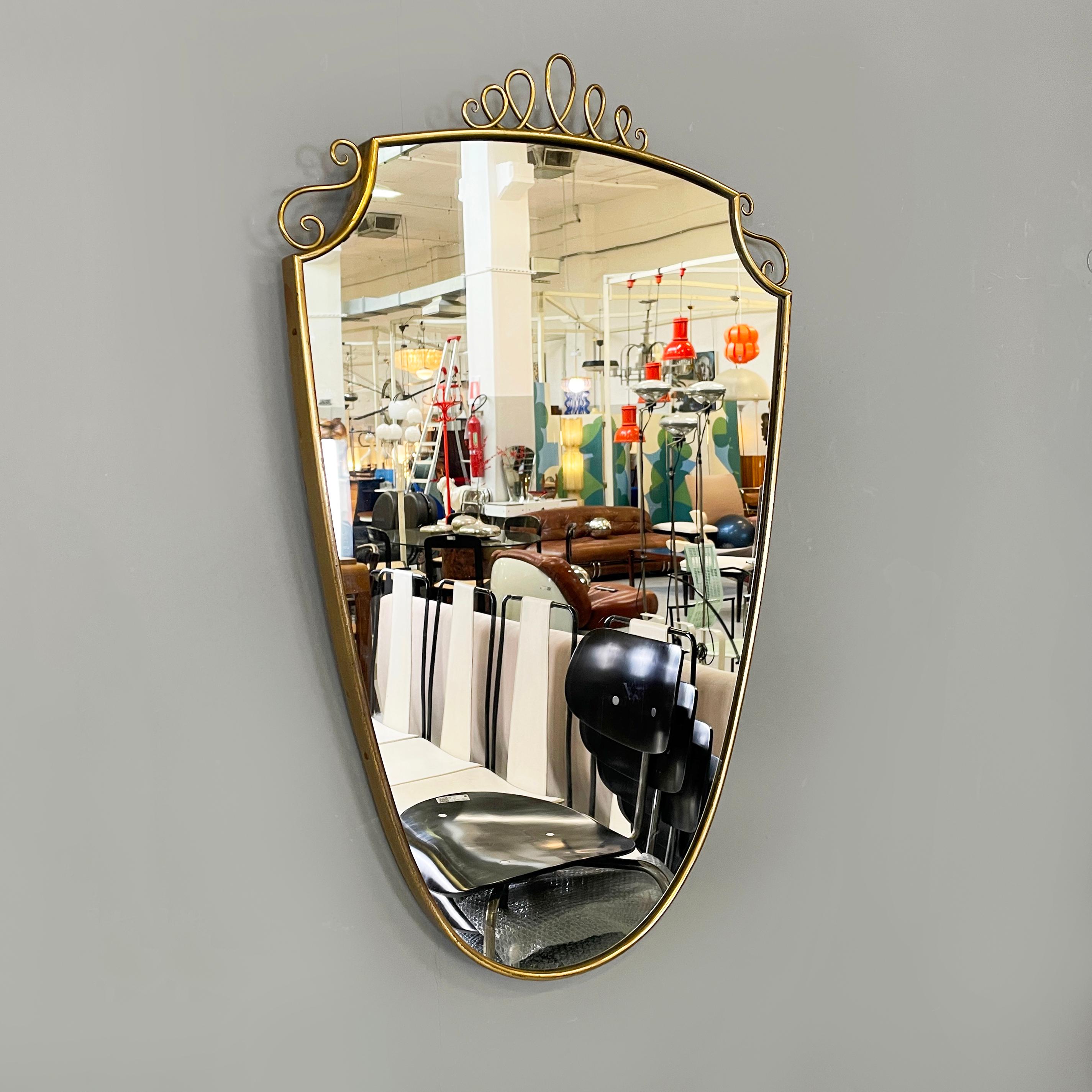 Italian mid-century modern Shield-shaped wall mirror with brass frame, 1950s
Shield-shaped wall mirror with brass frame. In the upper part it has two specular decorations on the corners and one in the center.
1950s
Good condition, shows signs of use