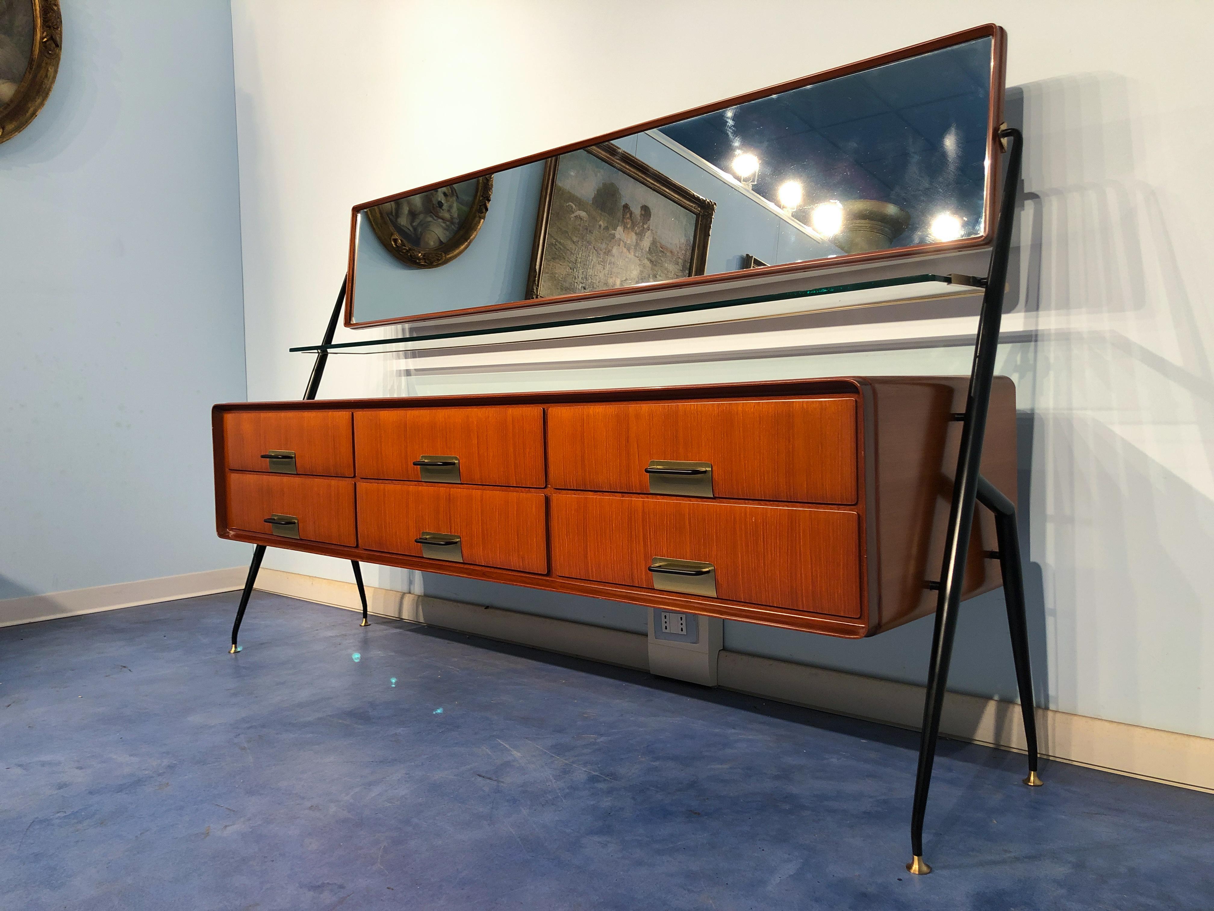 Stylish Italian sideboard-vanity dresser designed by Silvio Cavatorta in 1955. The cabinet is in teak wood, equipped with six drawers and finished with brass details, surmounted by a fixed glass shelf trimmed in brass and a swivel mirror. All rising