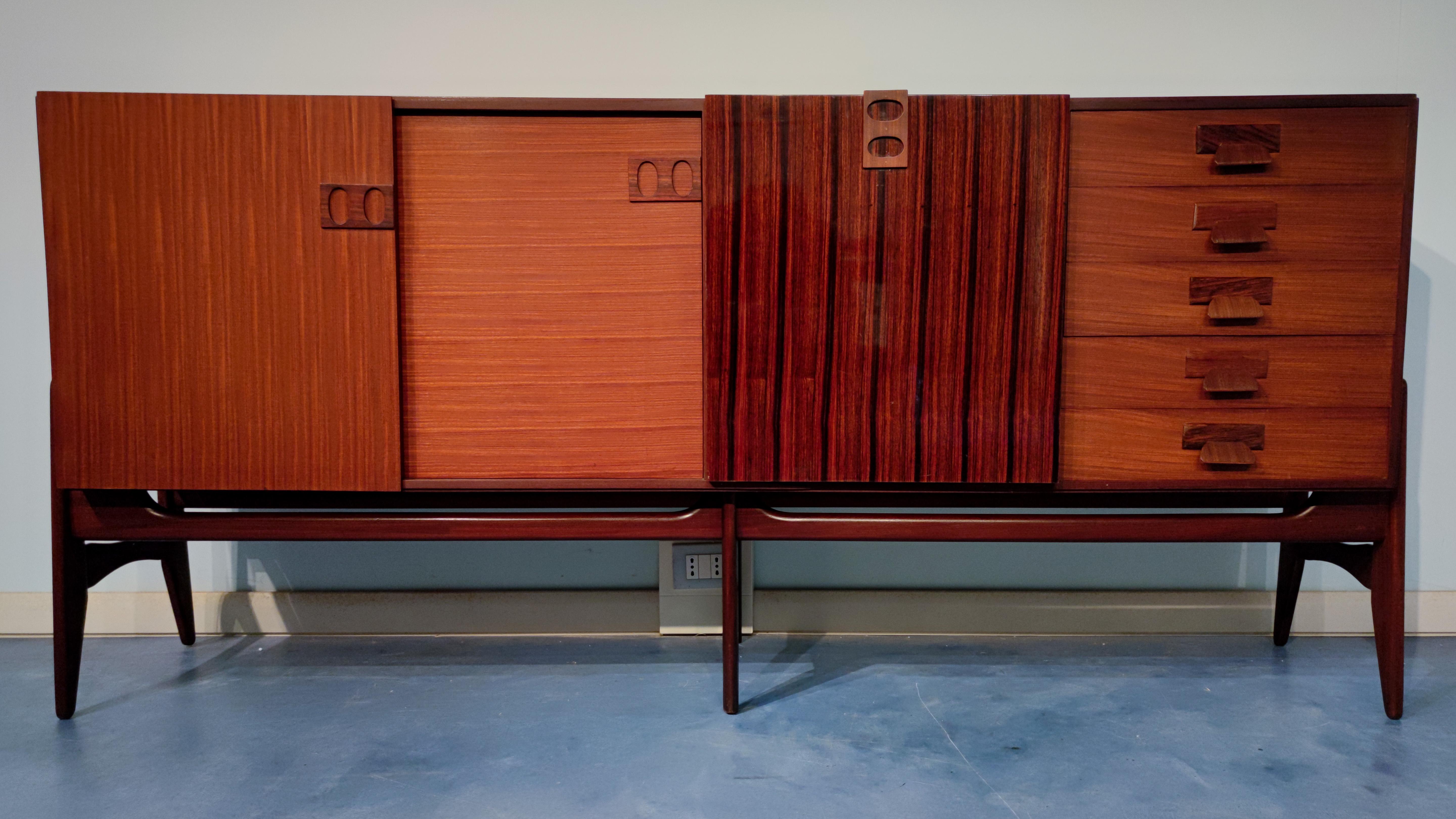 This Italian sideboard has details that reveal the craftsmanship involved in its production. The front composition of two sliding doors in horizontal and vertical wood grain, the central glossy finish door used as a bar and five drawers with