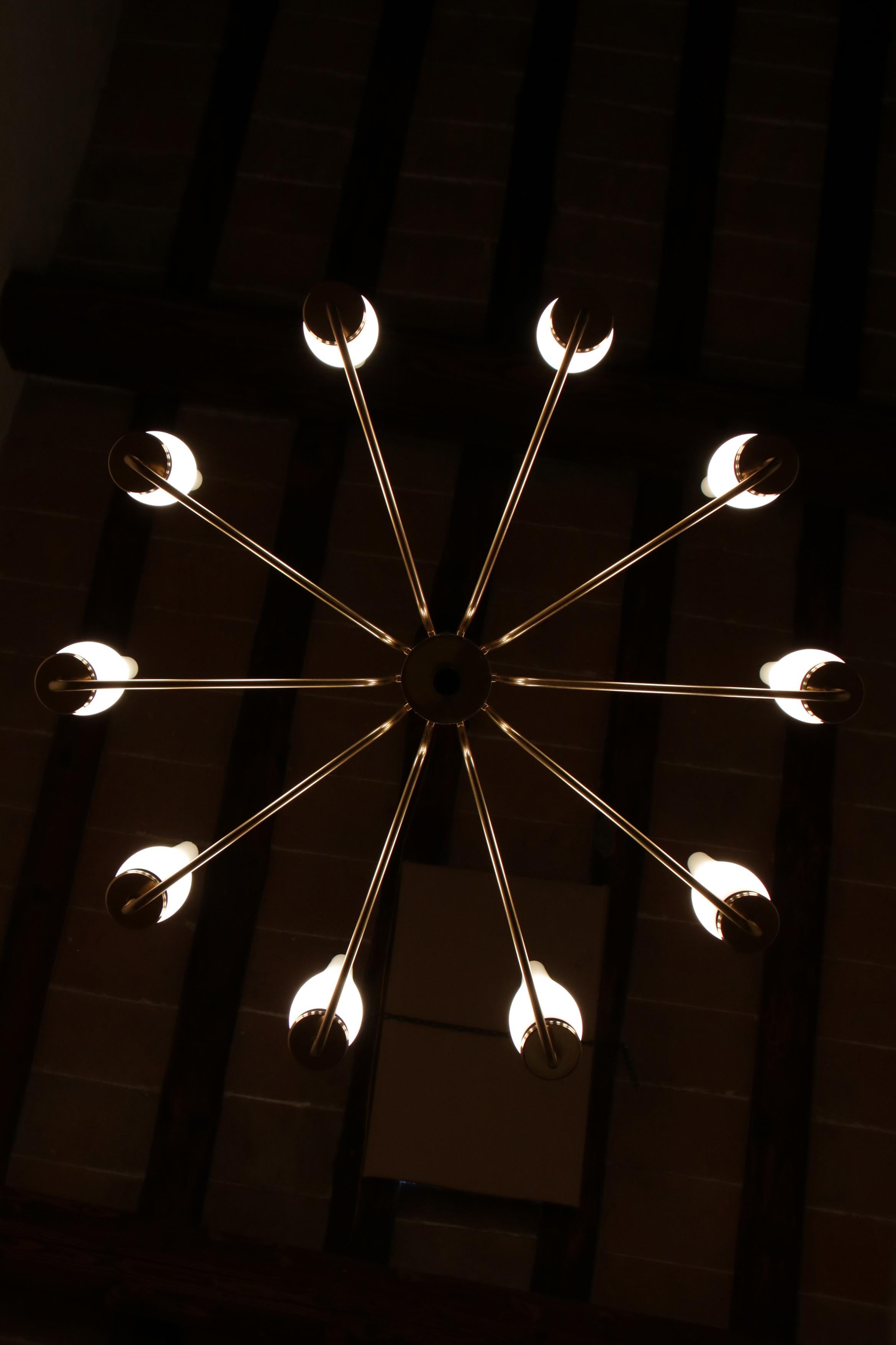 Bellissimo lampadario italiano Mid-Century Modern a dieci luci in formato E14, attribuito alla manifattura Stilnovo, risalente agli anni '50. Il lampadario è realizzato in ottone lucido, alluminio verniciato nero e vetro opalino. La grande qualità