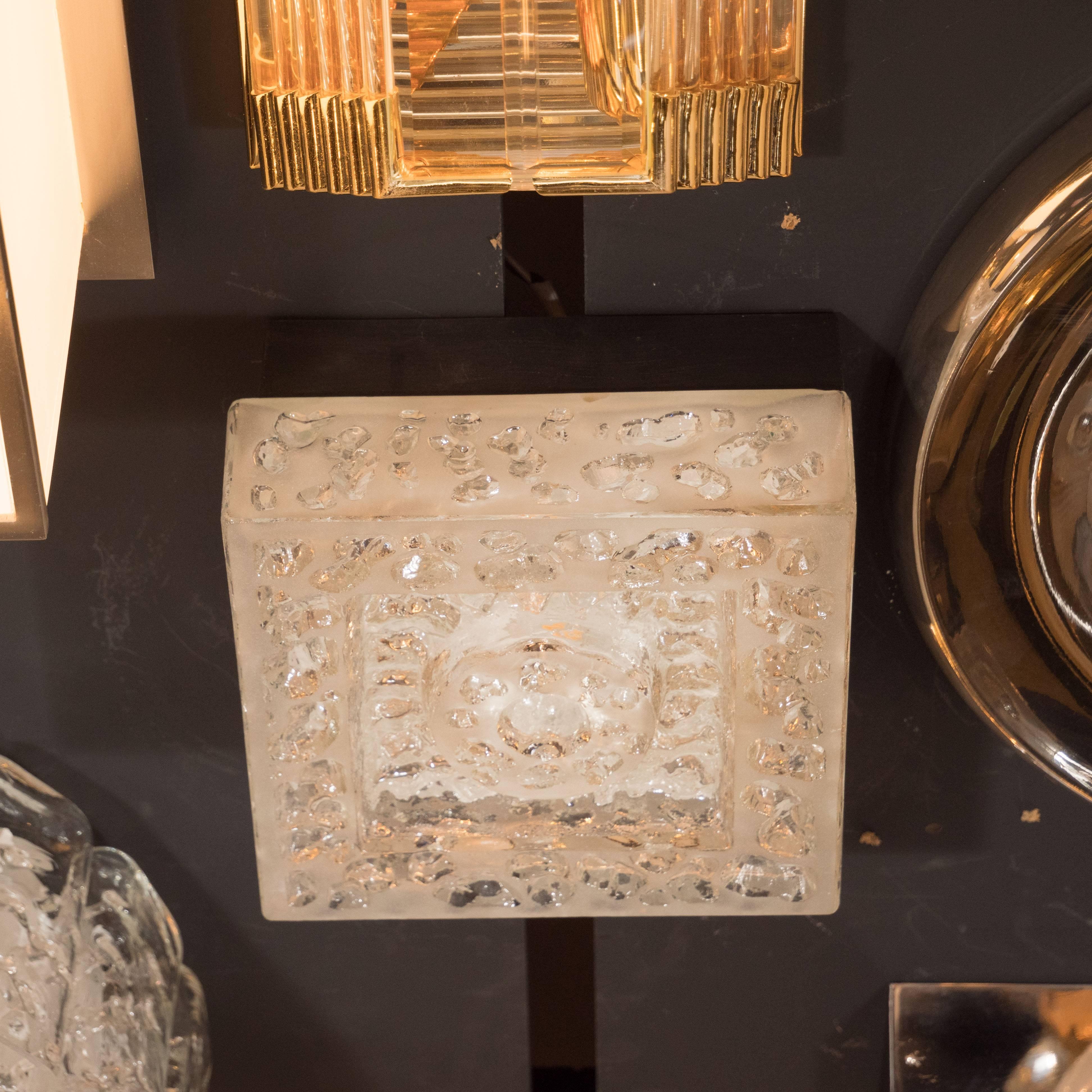 This exquisite flush mount was realized by the illustrious lighting studio, BEGA, in Italy, circa 1960. It features a square glass body with a depression in the center from which a circular form protrudes- all in intricately textured glass offering