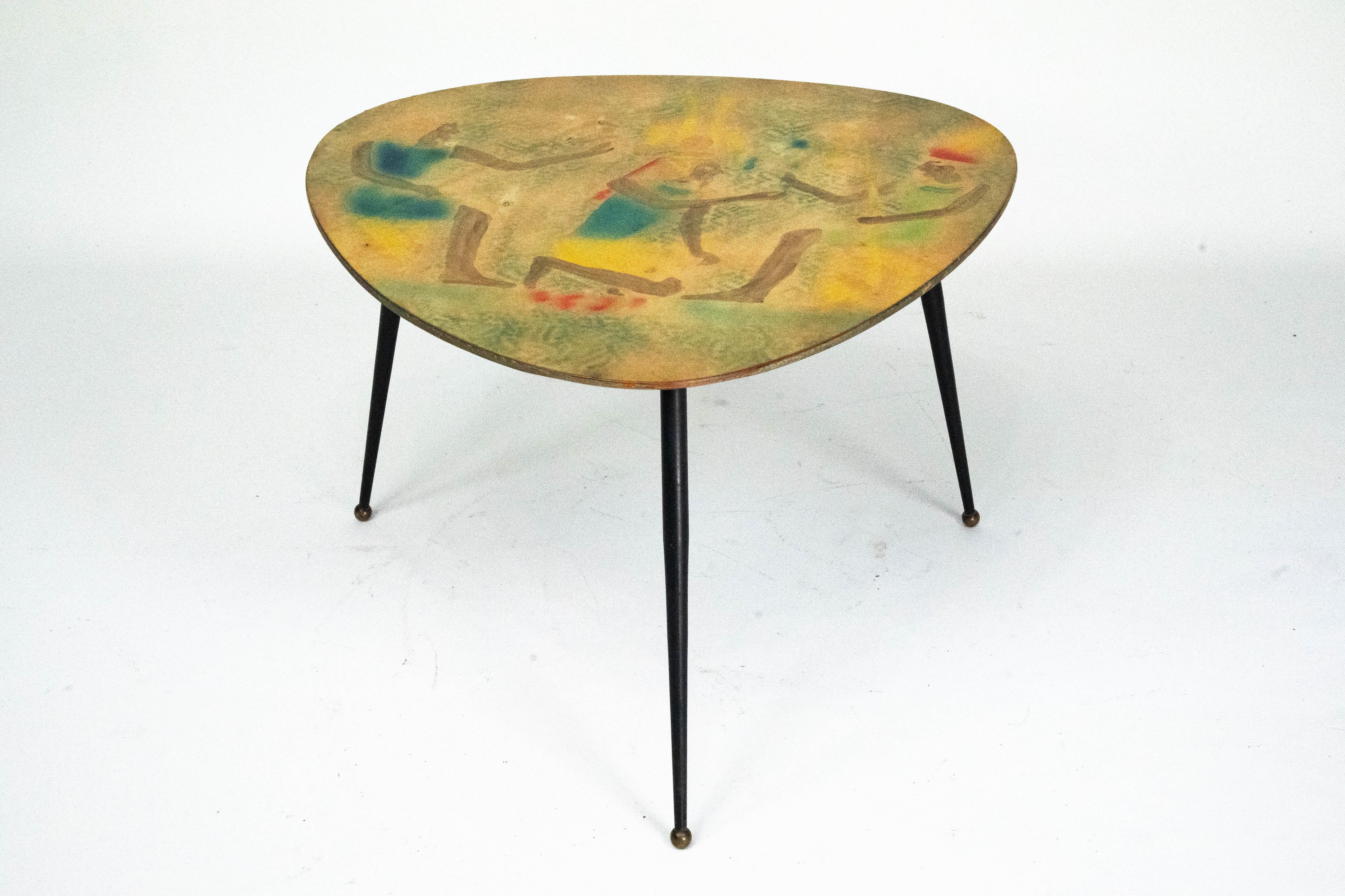 Elegant Italian mid-century modern low coffee table dating from the 1950s.
The table features an organically shaped top with a finely decorated surface, characterized by abstract motifs and warm earthy tones punctuated by subtle accents of blue,