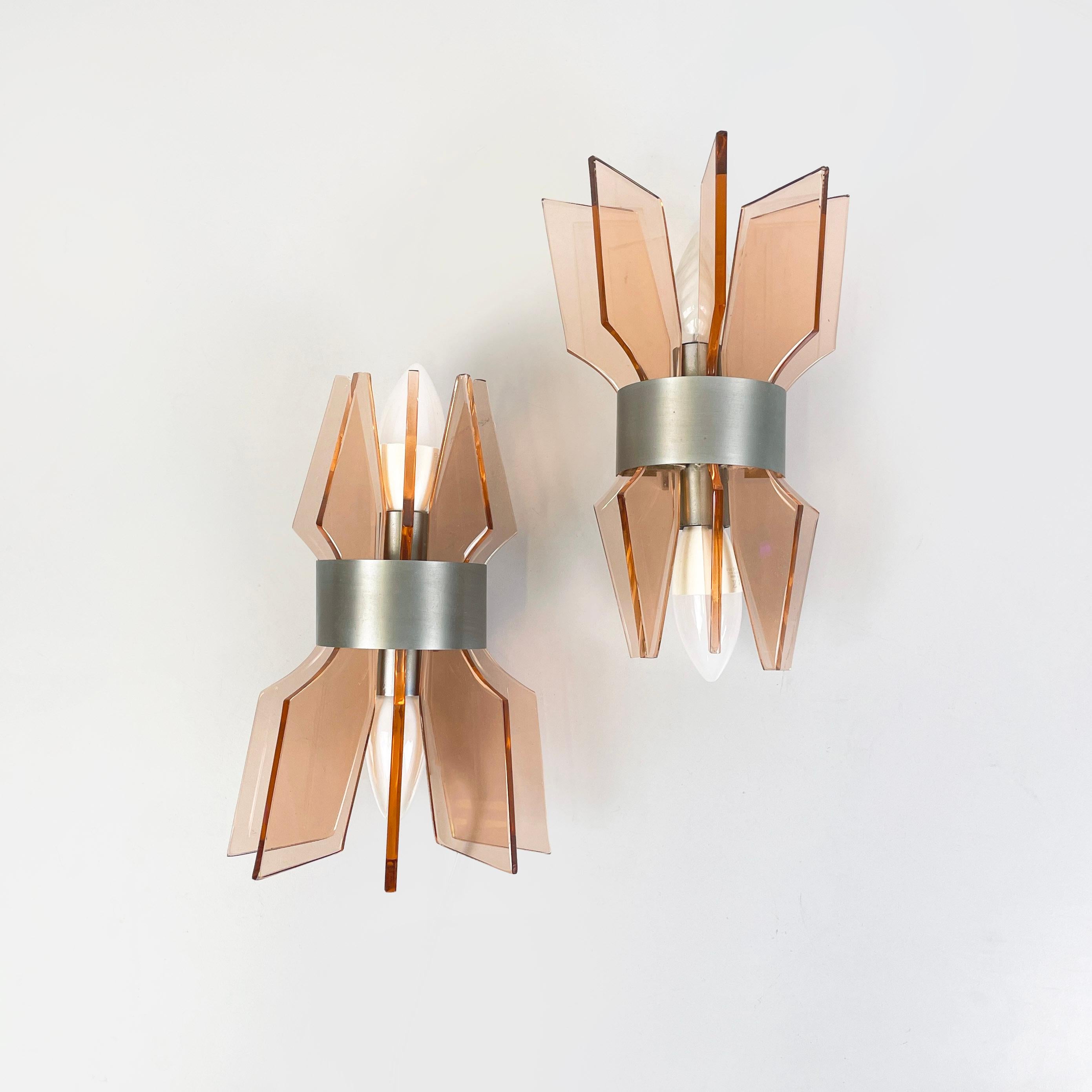 Italian mid-century modern Wall lamps in peach pink glass and metal, 1960s
Pair of wall lamps with double light source. The diffuser is made up of five peach-pink geometric glass plates, which narrow in the centre. The structure is composed of a