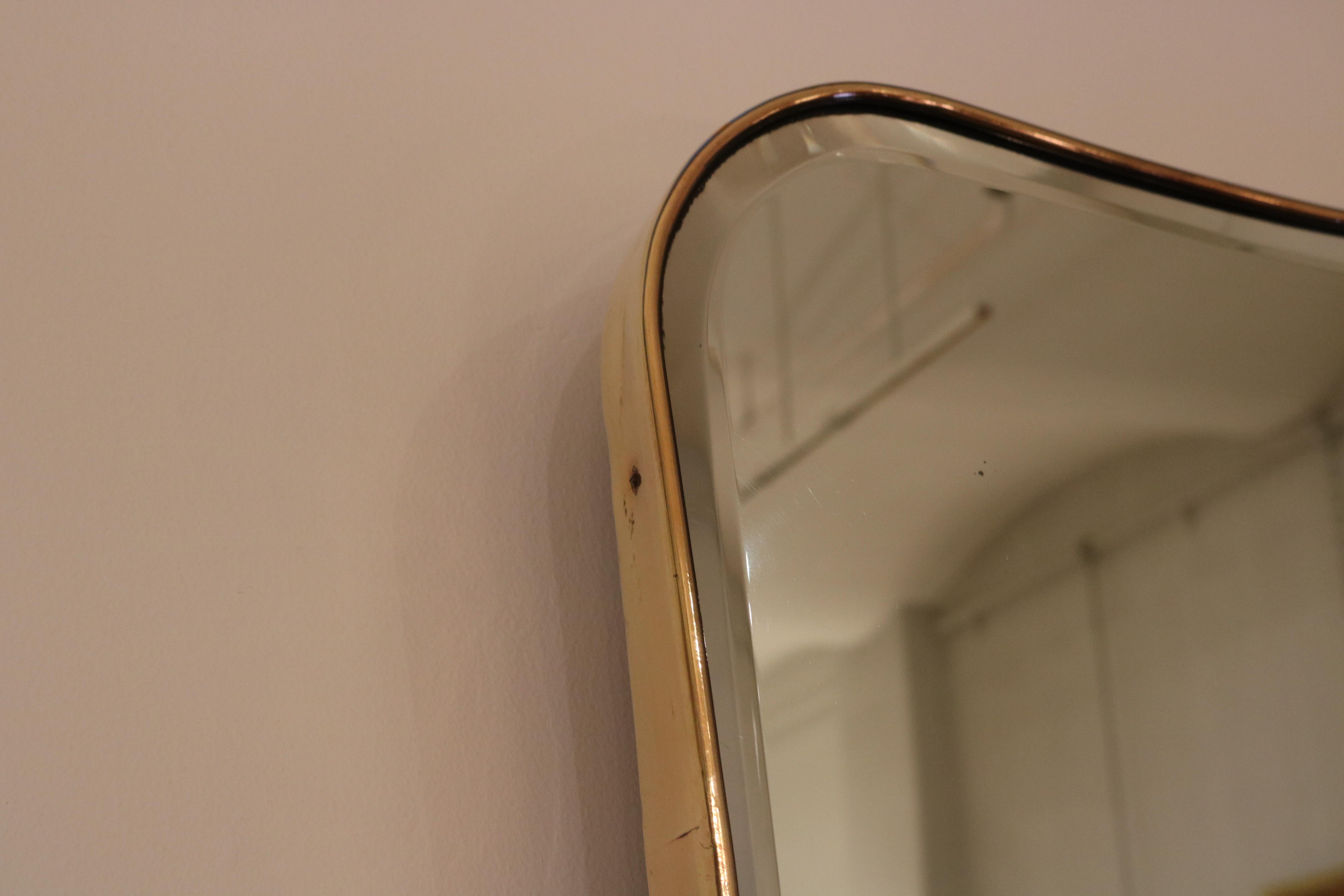 Ein italienischer Wandspiegel der Jahrhundertmitte mit geschwungenem Oberteil und Messingrahmen. Der Spiegel zeigt die originale Spiegelscheibe mit abgeschrägter Kante.
