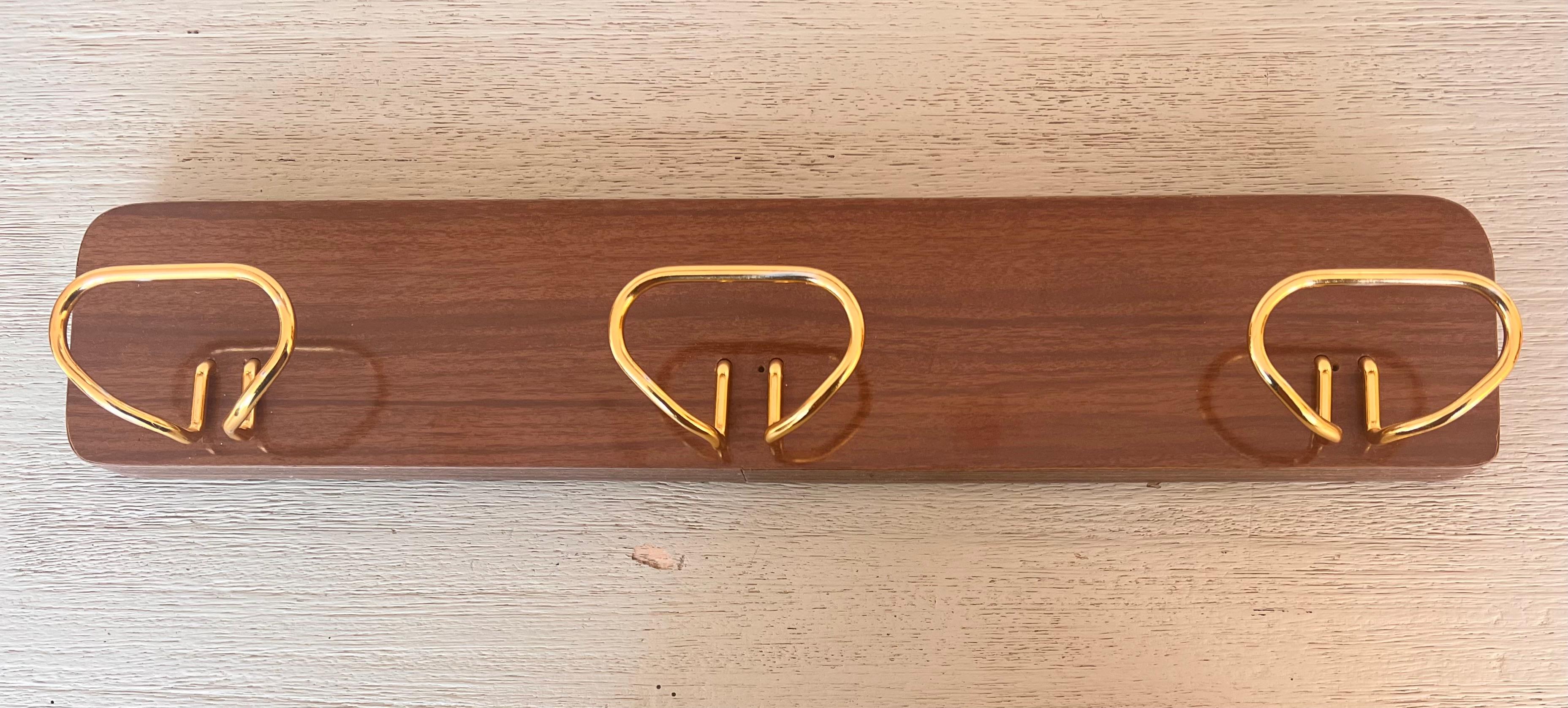 Italian Mid-Century Modern wooden structure and three brass hooks wall coat hanger. Elegant wall coat hanger, with four brass hooks with a typical midcentury and sixties design. Even the screws and the attachment of the hooks to the wooden strips