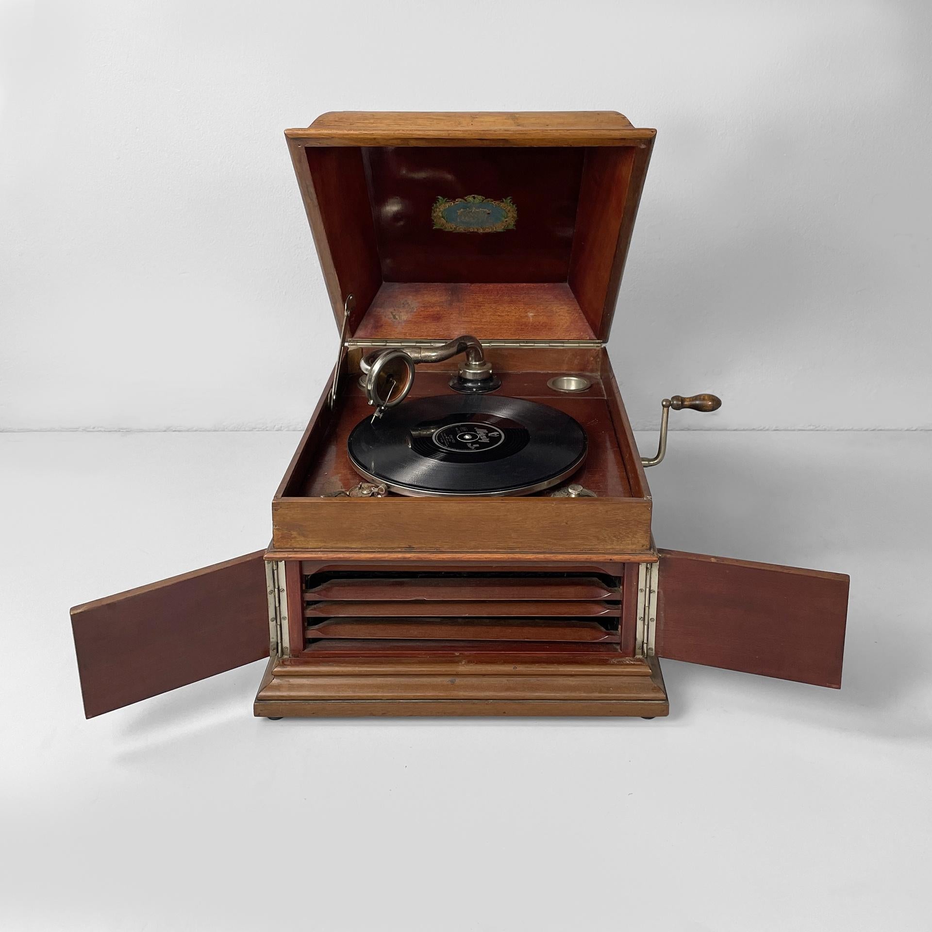 Grammofono italiano in legno e metallo della metà del secolo scorso di C.C., anni '40
Fantastico grammofono da tavolo vintage con struttura in legno e due raccolte di dischi con ventidue dischi. All'interno c'è un giradischi rivestito in tessuto