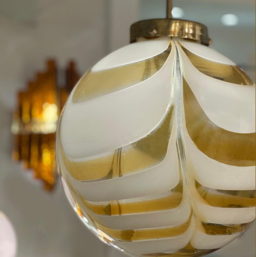 This chic pendant fixture is a mid-century Modern work of art. It features a handcrafted Murano glass globe with soft amber and white lattimo glass in an alternating ribbon pattern. This arrangement of opaque and translucent glass captures and