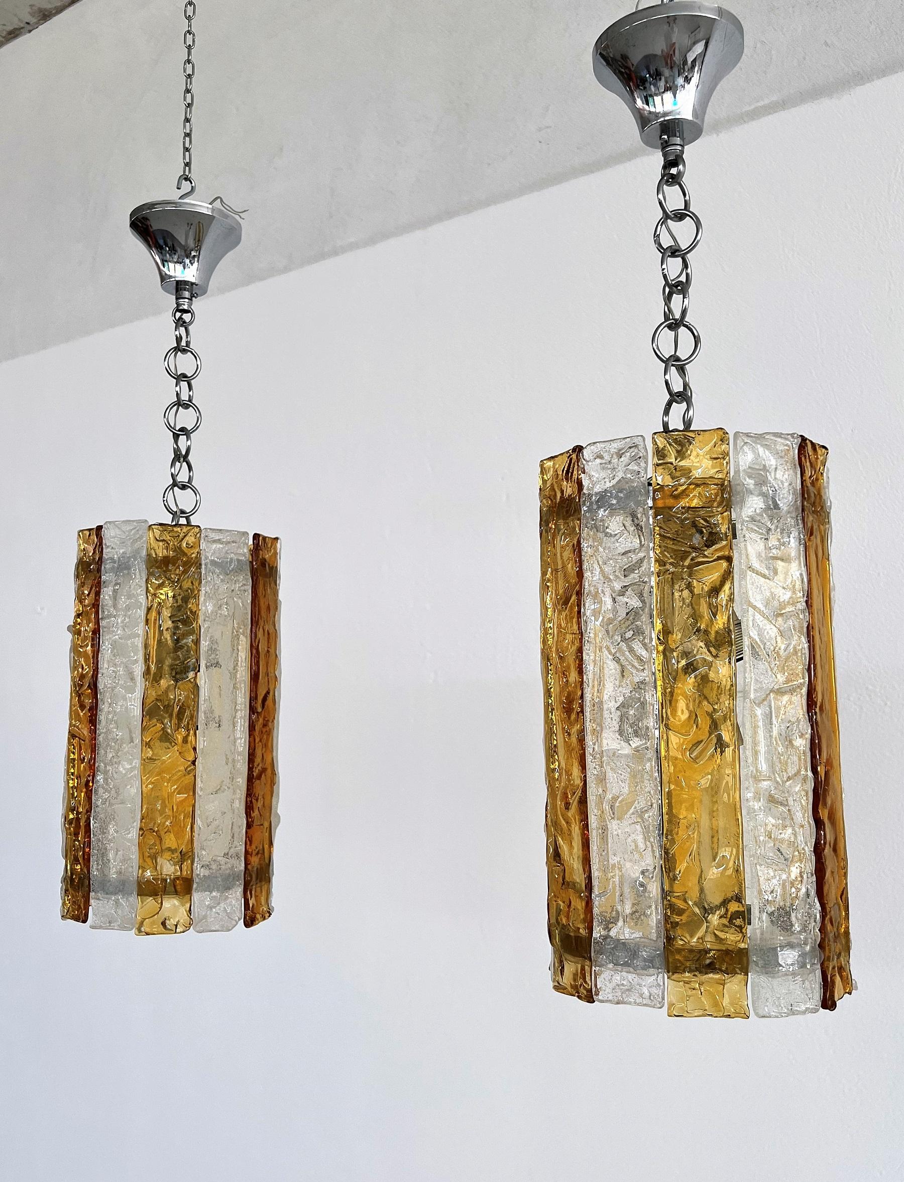 Gorgeous set of two pieces of heavy pendant lights in two-tone yellow-transparent glass strips.
Made in Murano by Mazzega during the 1960s.
The glass is stunning to see and much better in person.
The pendants base is made of strong chromed metal,