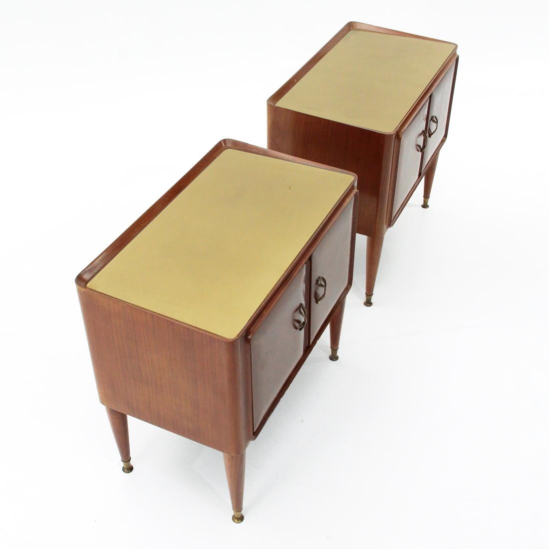 Pair of Italian-made bedside tables produced in the 1950s.
Veneered wooden structure with rounded corners.
Back painted glass top.
Veneered wooden doors with convex front surface and brass handles.
Turned legs in solid wood with brass