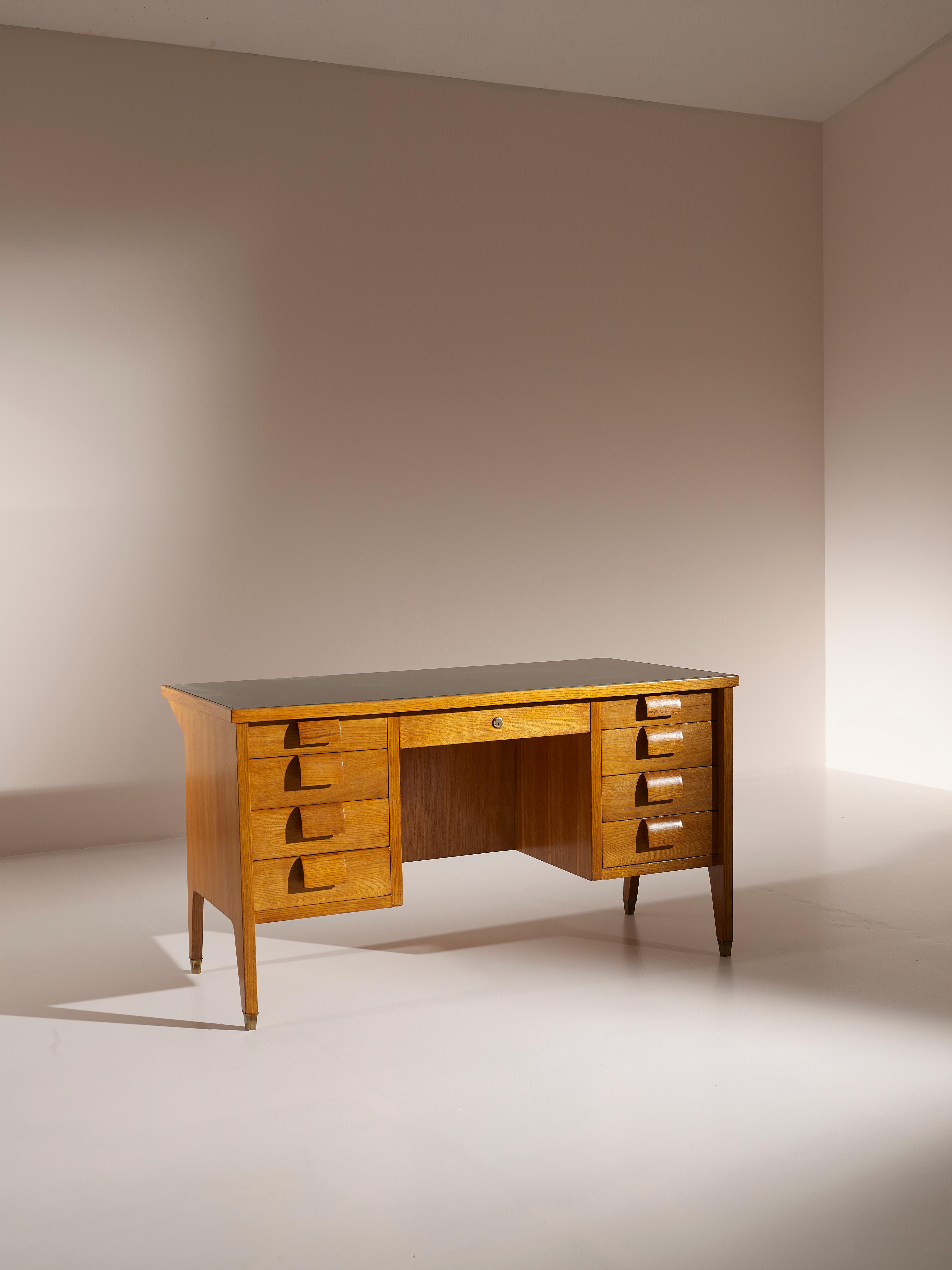 An executive desk produced in Italy in the 1950s with a beautiful design which reminds some Gio Ponti works.

Made in solid oak, this desk features eight side drawers with powerful, carved handles, a central drawer with key, a green glass top and