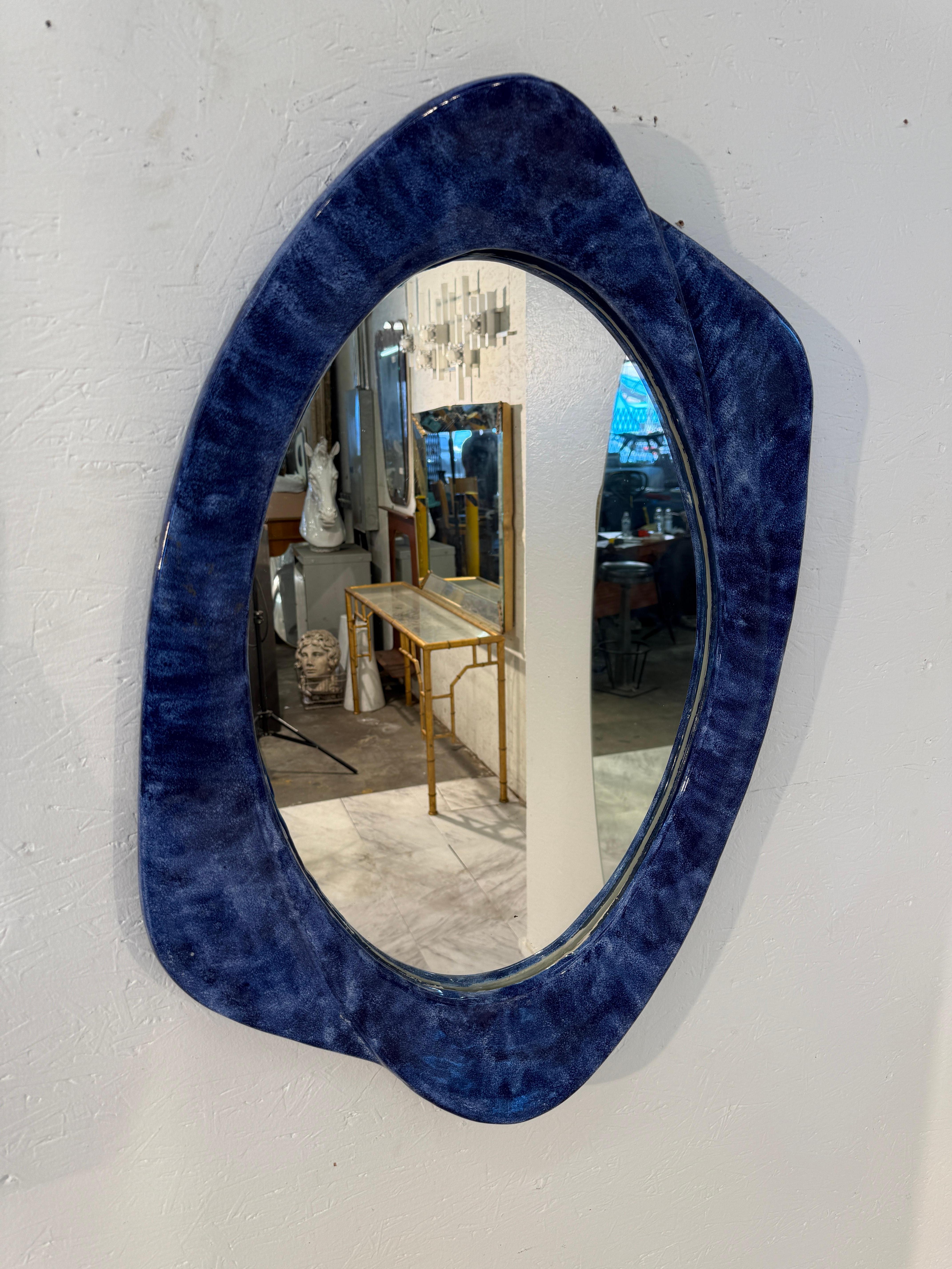 Miroir italien des années 1970, se distinguant par son cadre organique sculptural en riche céramique bleue. La forme doucement ondulée rappelle les lignes fluides et asymétriques typiques du design italien du milieu du siècle dernier, où la fonction
