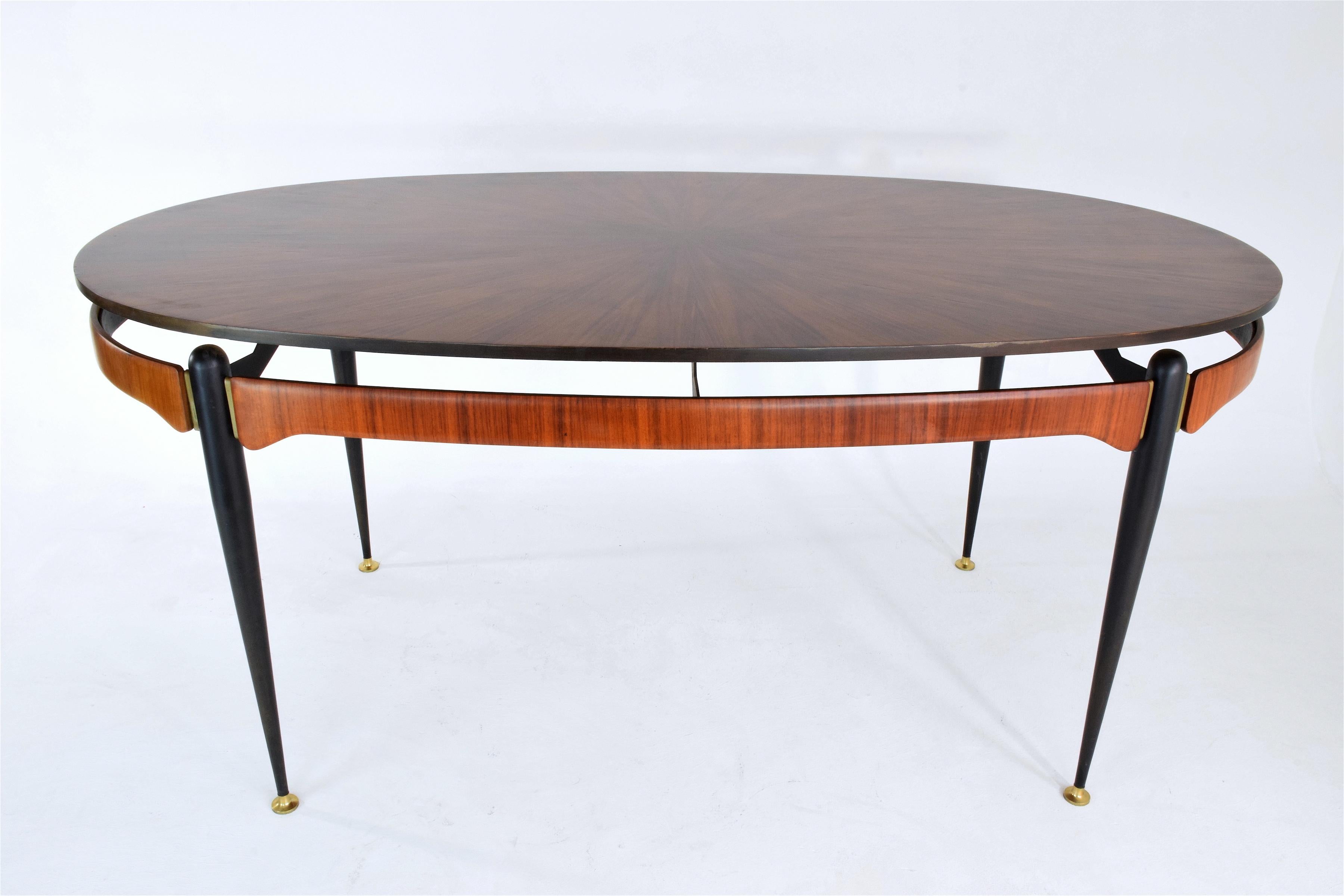A beautiful collectible Italian vintage 6 seater oval wood dining table of striking design in teak veneer, tapered legs composed of black lacquered steel and adorned with brass endings, 
Italy, circa 1950s.
 ----
All our pieces are fully restored at