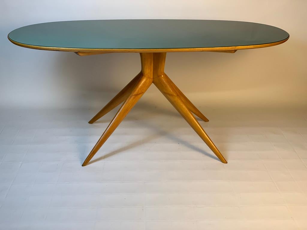 Oval table with recessed green back-painted glass top, made in Italy in the 1950s, Mid-Century Modern with a stylized structure in light wood consisting of four thin legs that cross under the top.
This can be a dining table, a center table or a