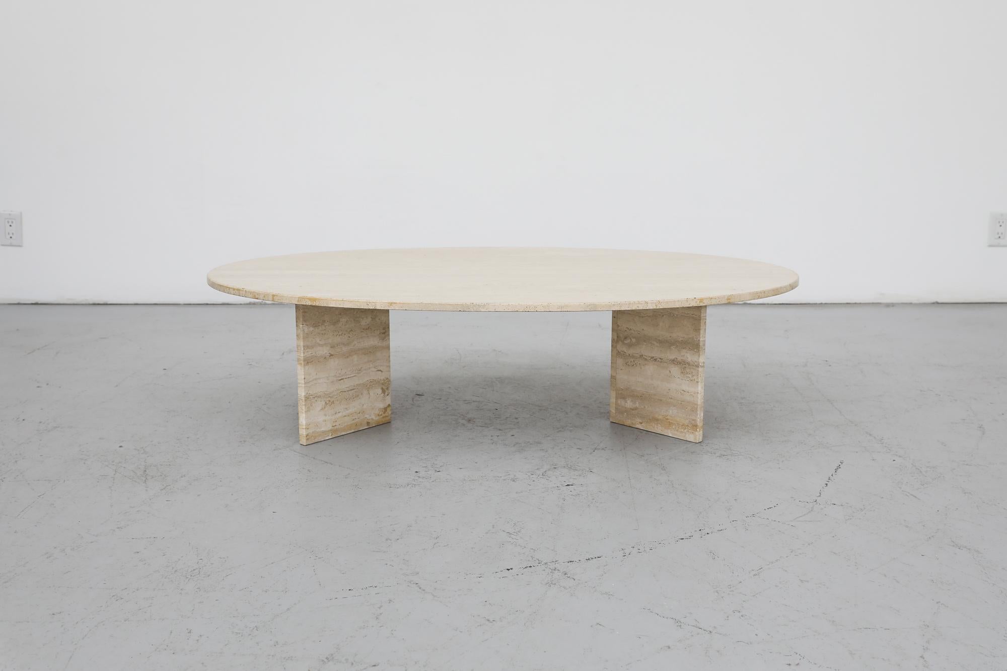 This Mid-Century solid oval travertine coffee table has an elegant Post Modern design. The heavy oval top sits loose on two v-shaped legs of the same material. One of the leg shows signs of previous repair. In original condition with visible wear