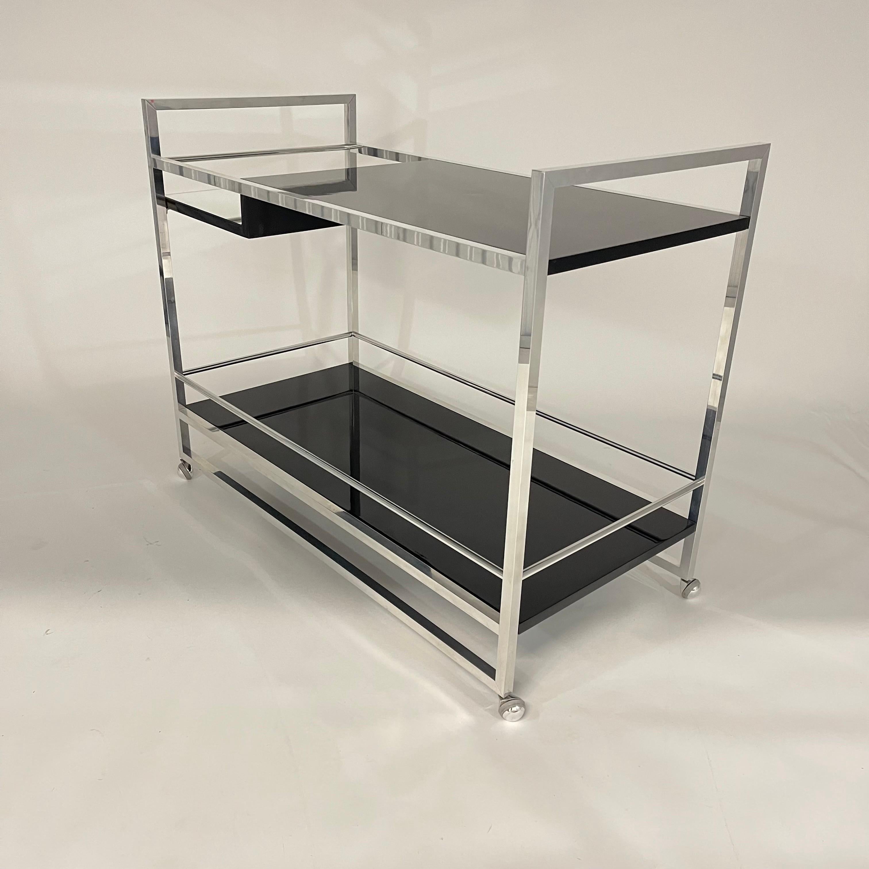 Mid-Century Bar Cart or Drinks Tea Trolley, rendered in a polished chrome frame with 3 levels of shelving, the bottom and top shelves in black lacquer with a middle bottle or ice bucket shelf in mirror, all supported in revolving castors. Italy,