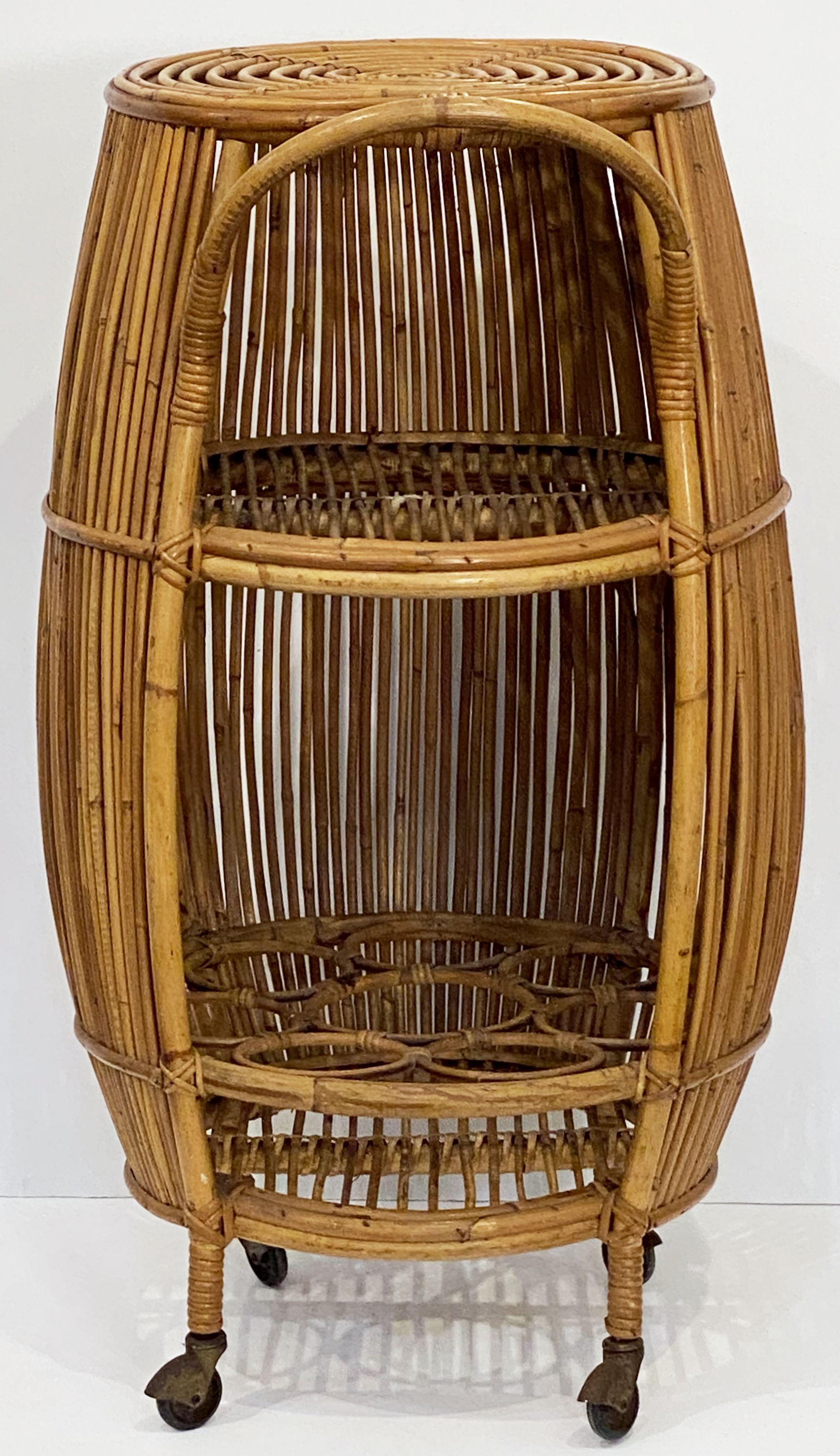 A fine Italian bar cart or trolley in rattan and bamboo from the 1960s, featuring a barrel-shaped design with curved handle, the top with a spiral design of rattan, an interior shelf, the base with fittings for bottles, set upon for rolling wheels.