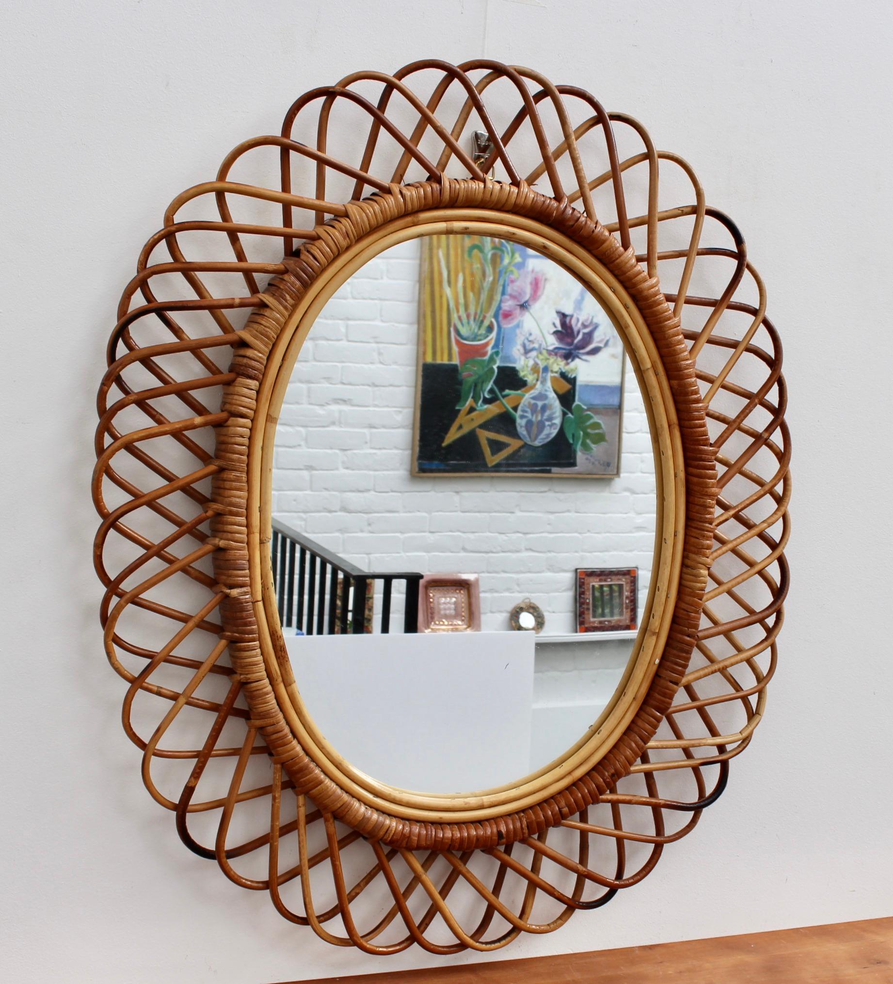 Italian rattan wall mirror, (circa 1960s). This piece has a complex weave of rattan in a continual series of horseshoe-shaped projections on the frame edge. There is a graceful, characterful patina on the frame rattan and cane commensurate with age.