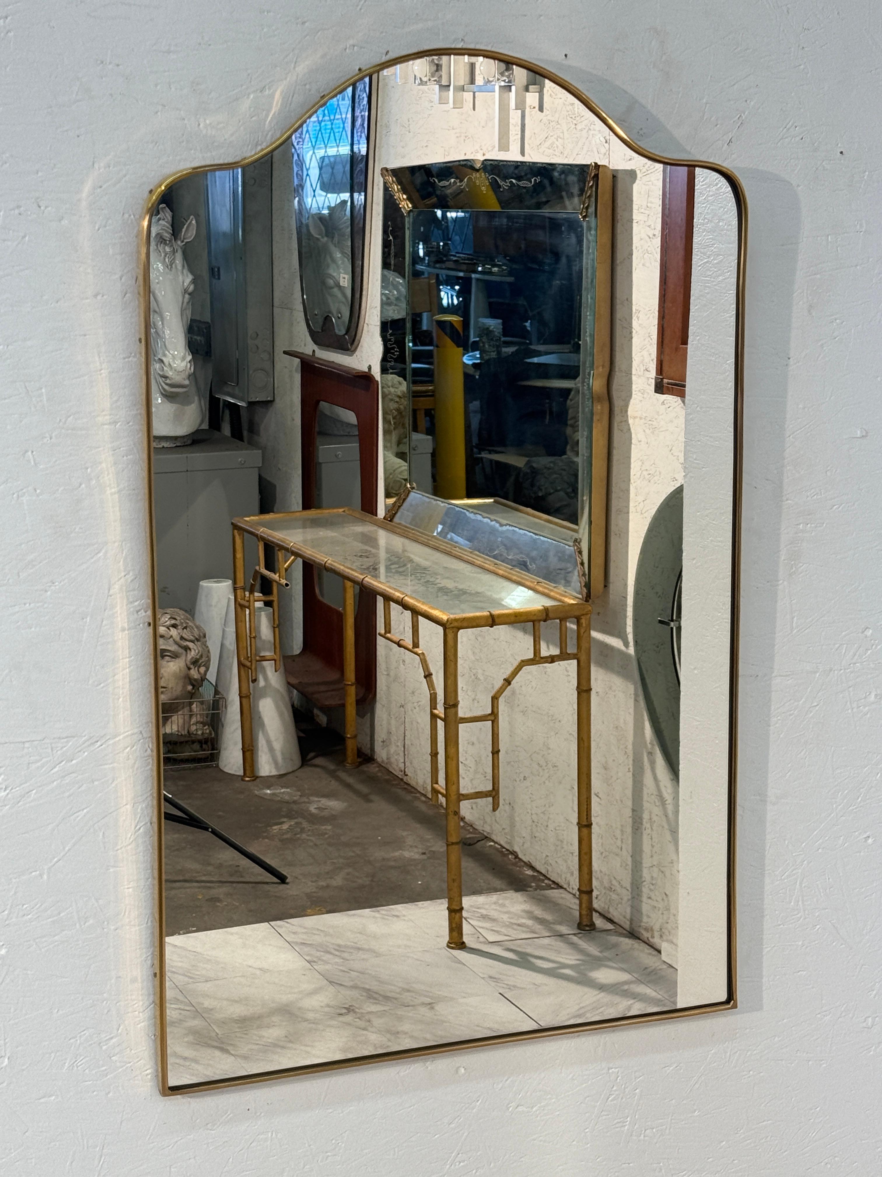 An  Italian mid-century wall mirror featuring a rectangular shape with a softly arched top. Framed in slim brass, the design balances clean lines with a graceful curve, embodying both simplicity and refinement.