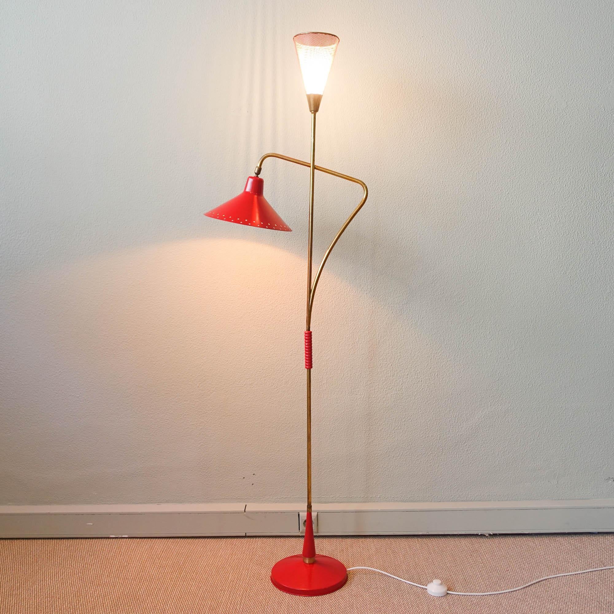 This double shade floor lamp was designed by Giuseppe Ostuni and produced in Italy during the 1950's. It has two metal shades, one in facing up in red perforated metal and the other, facing down in red, that are attached to a brass arm. With an