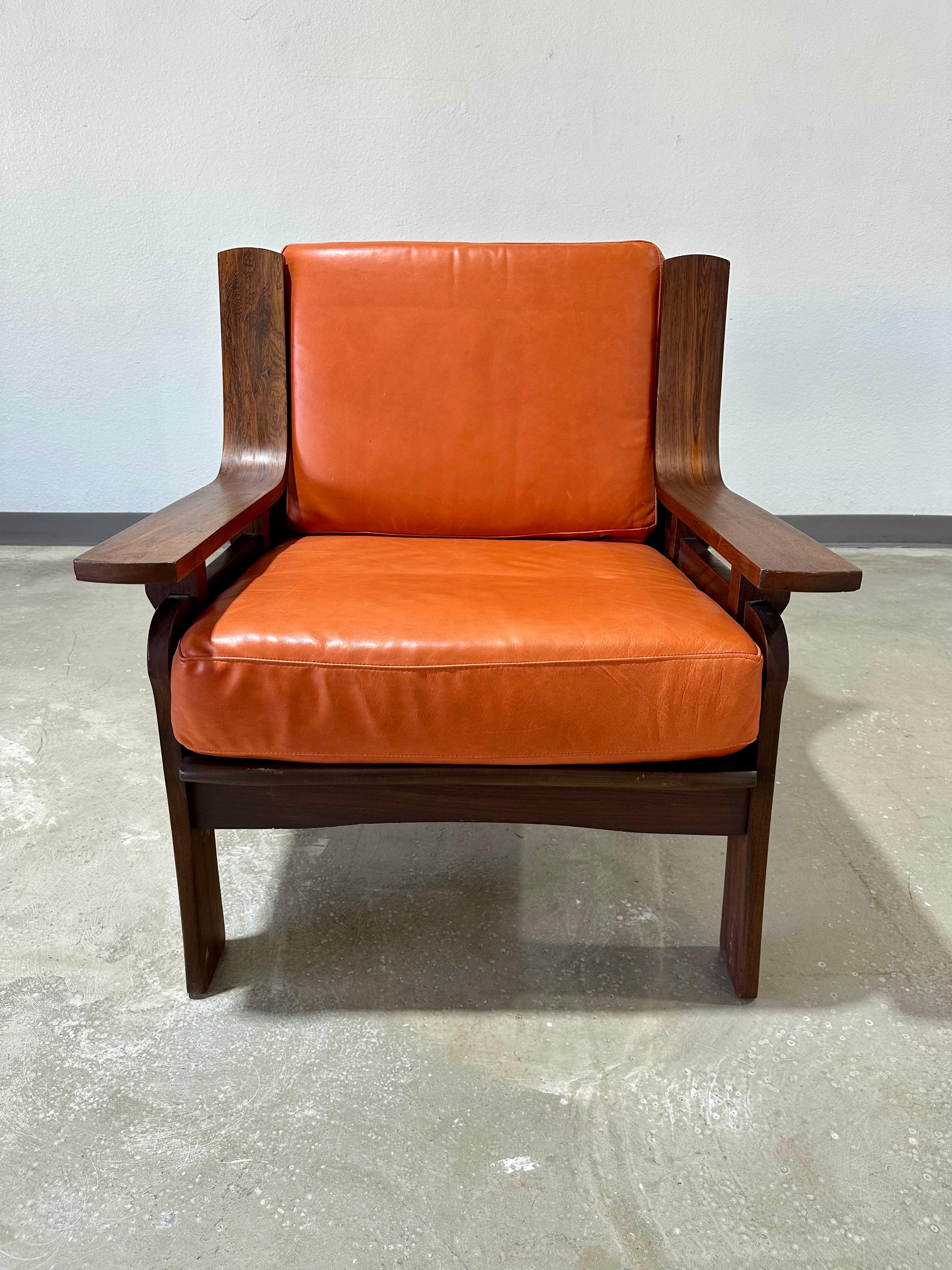Italian Mid Century Modern Lounge Chair Circa 1960’s. Rosewood frame with interesting shape and joinery, new cushions made within past two years in orange leather. Sweeping arms with floating effect, and slatted back. An attractive and comfortable