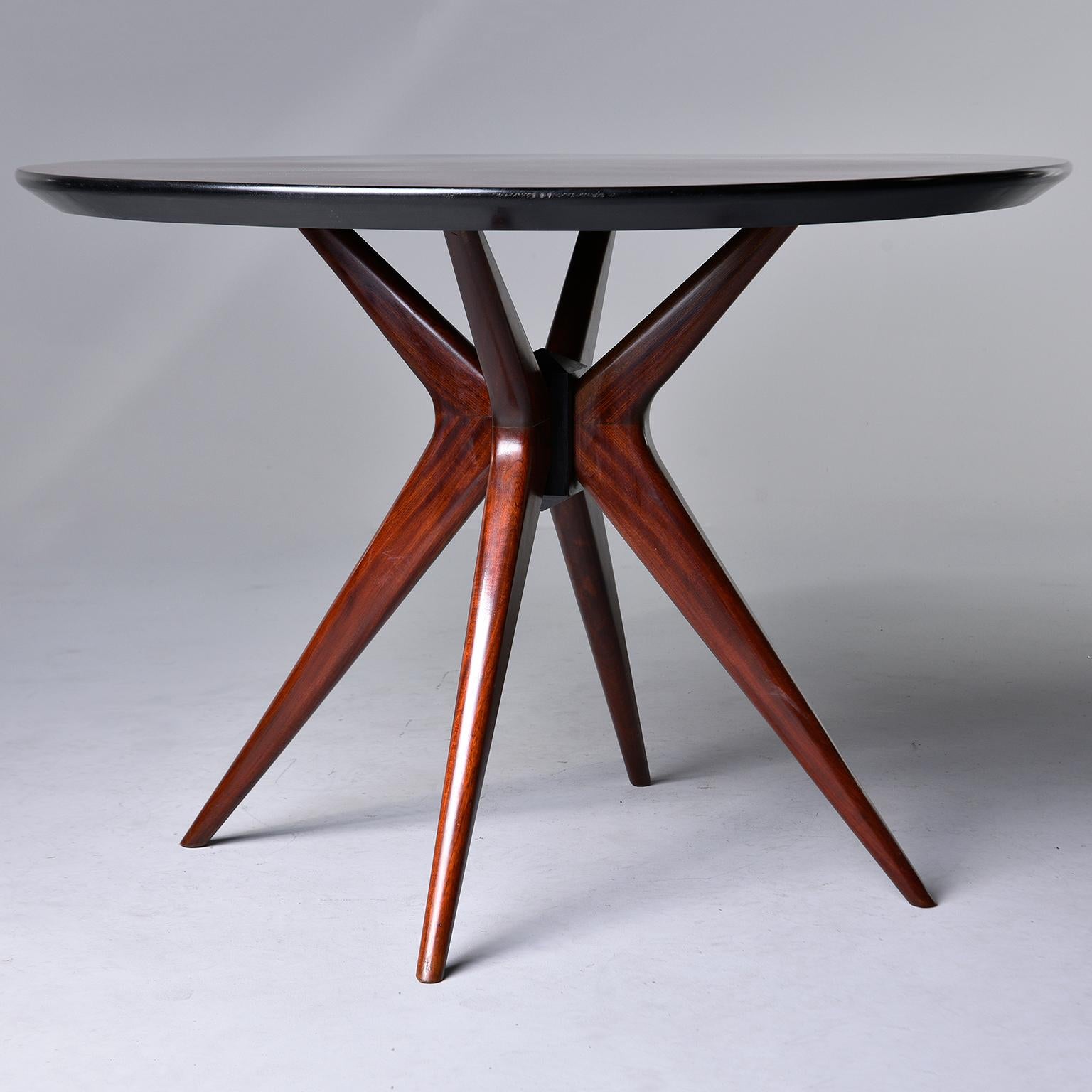 Italian center, breakfast or game table has a round top with rosewood veneer arranged so that the graining forms a star burst pattern, circa 1960s. The base of the table consists of four tapered, boomerang-shaped legs. Unknown maker.