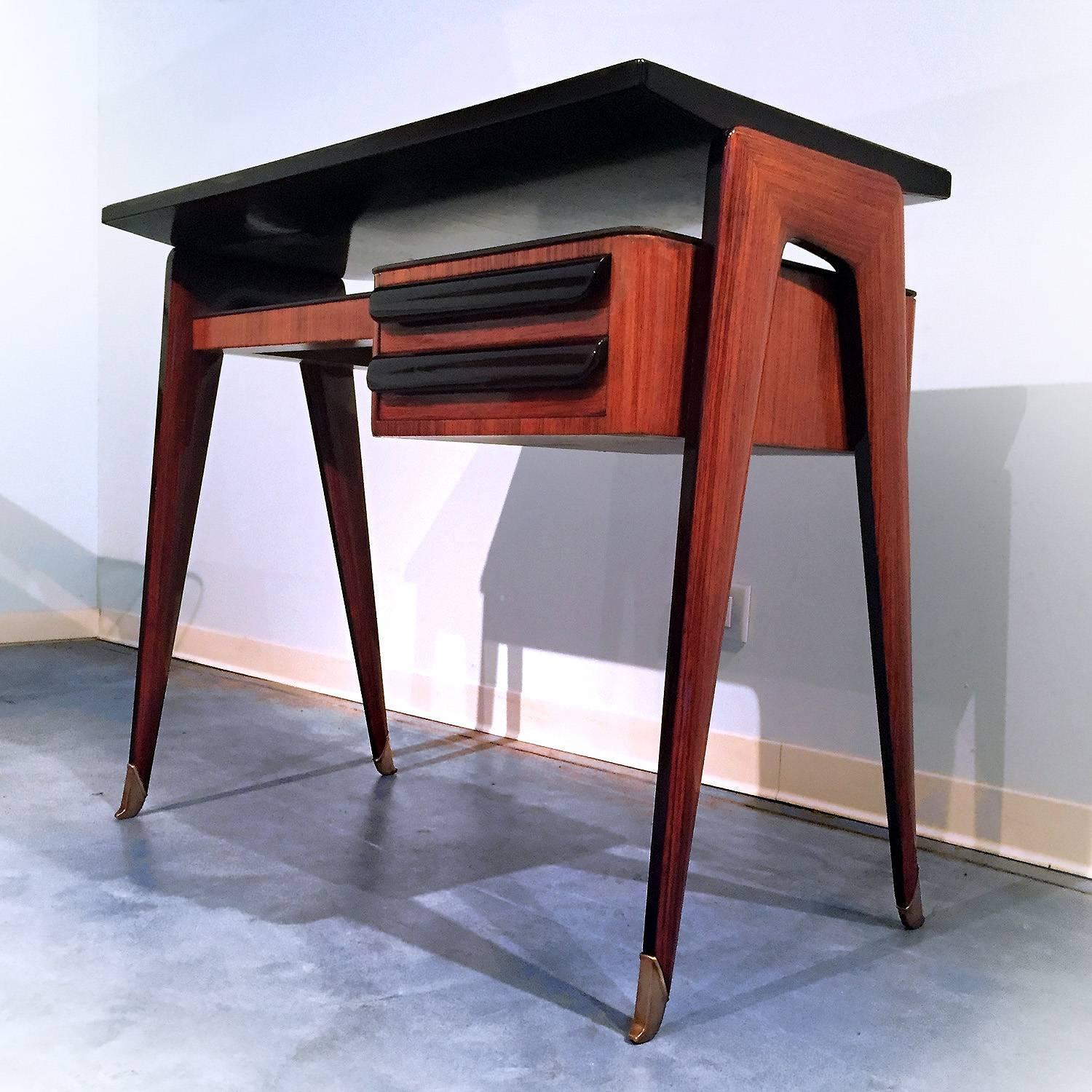 This stylish Italian petite desk, elegantly named 'dattilo', was designed by Vittorio Dassi in the 1950s.
The rosewood veneer structure is provided with green glass top and shelf with two drawers, finished with brass sabots.
Narrow depth makes this