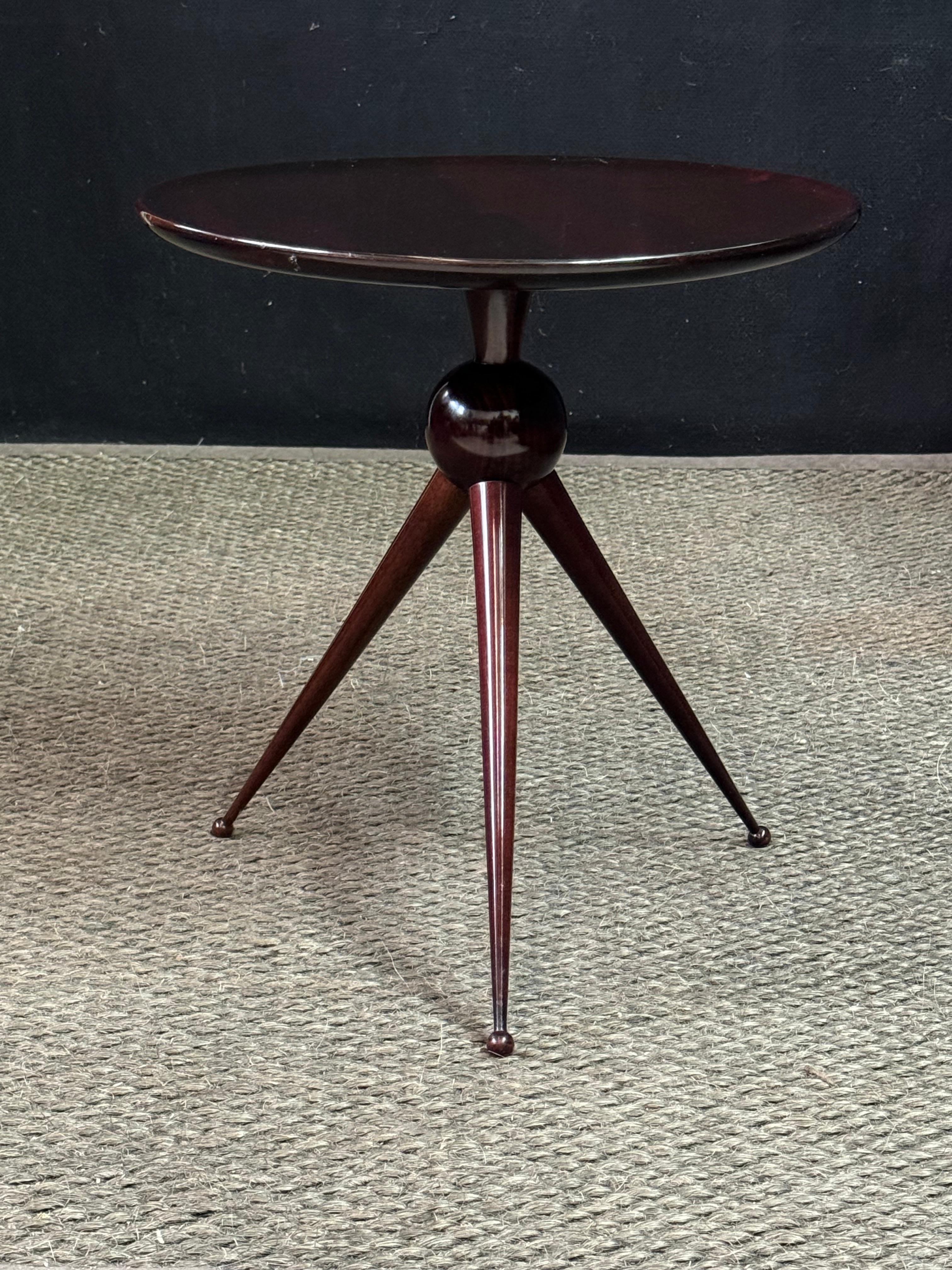 A tripod accent table designed by Cesare Lacca for Angelo De Baggis, originating from the late 1950s and a stunning example of Italian Mid-Century design. A round top with a concave edge is supported by a central pedestal over a sphere that has